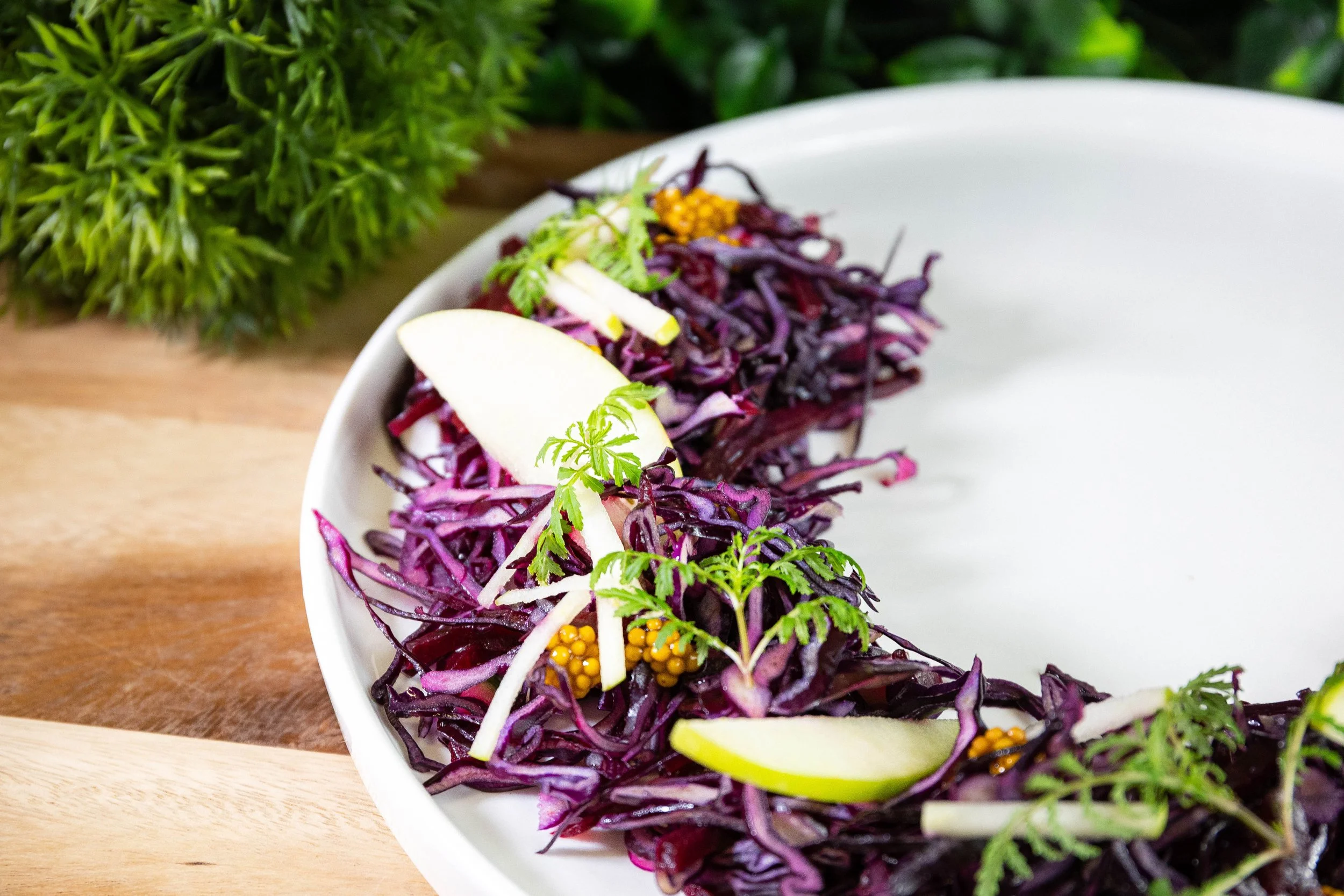 Salade de chou violet garnie de tranches de pomme et de petites fleurs, servie sur une assiette blanche.