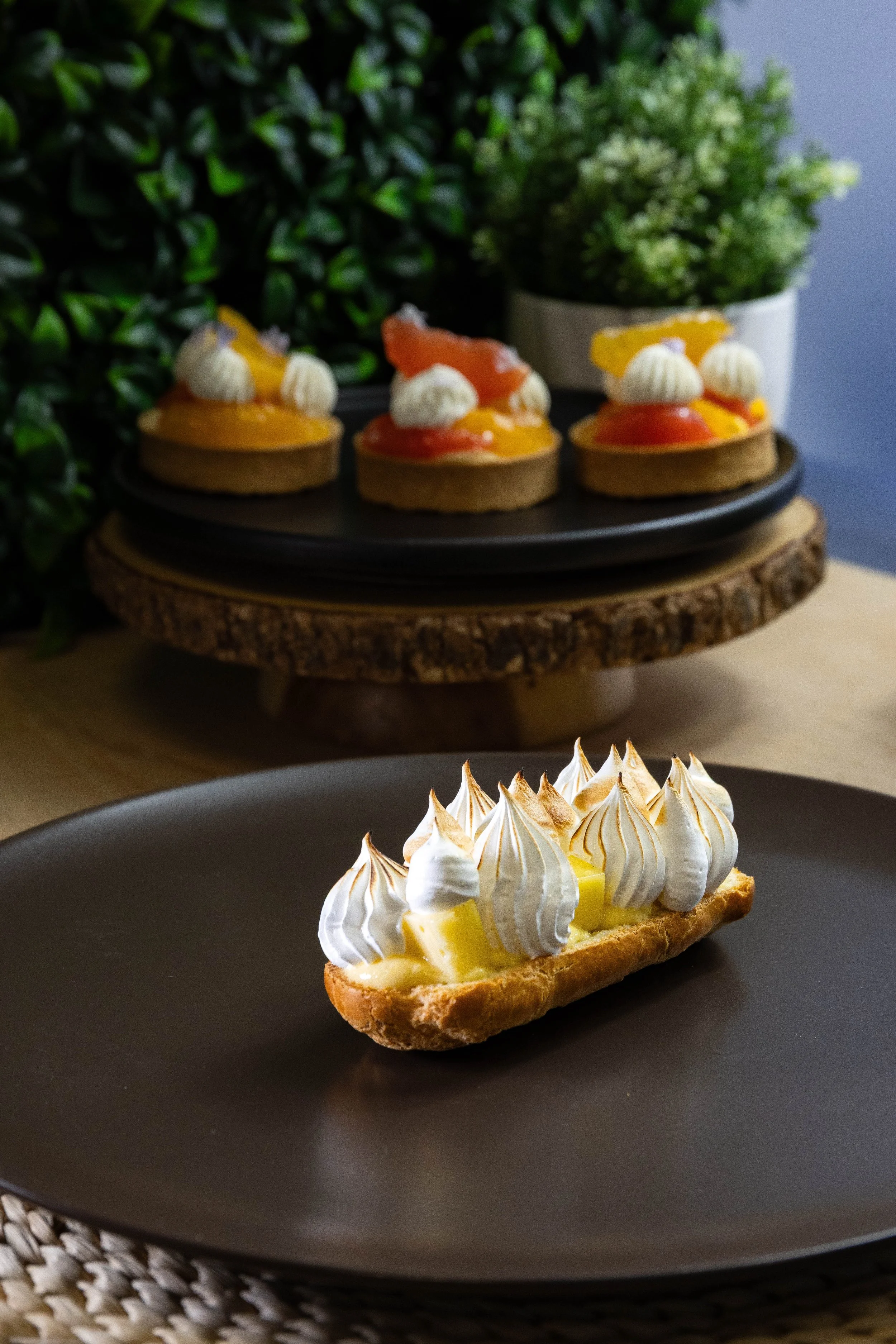 Tartelette crémeuse aux fruits jaunes et meringue dorée sur un fond noir.