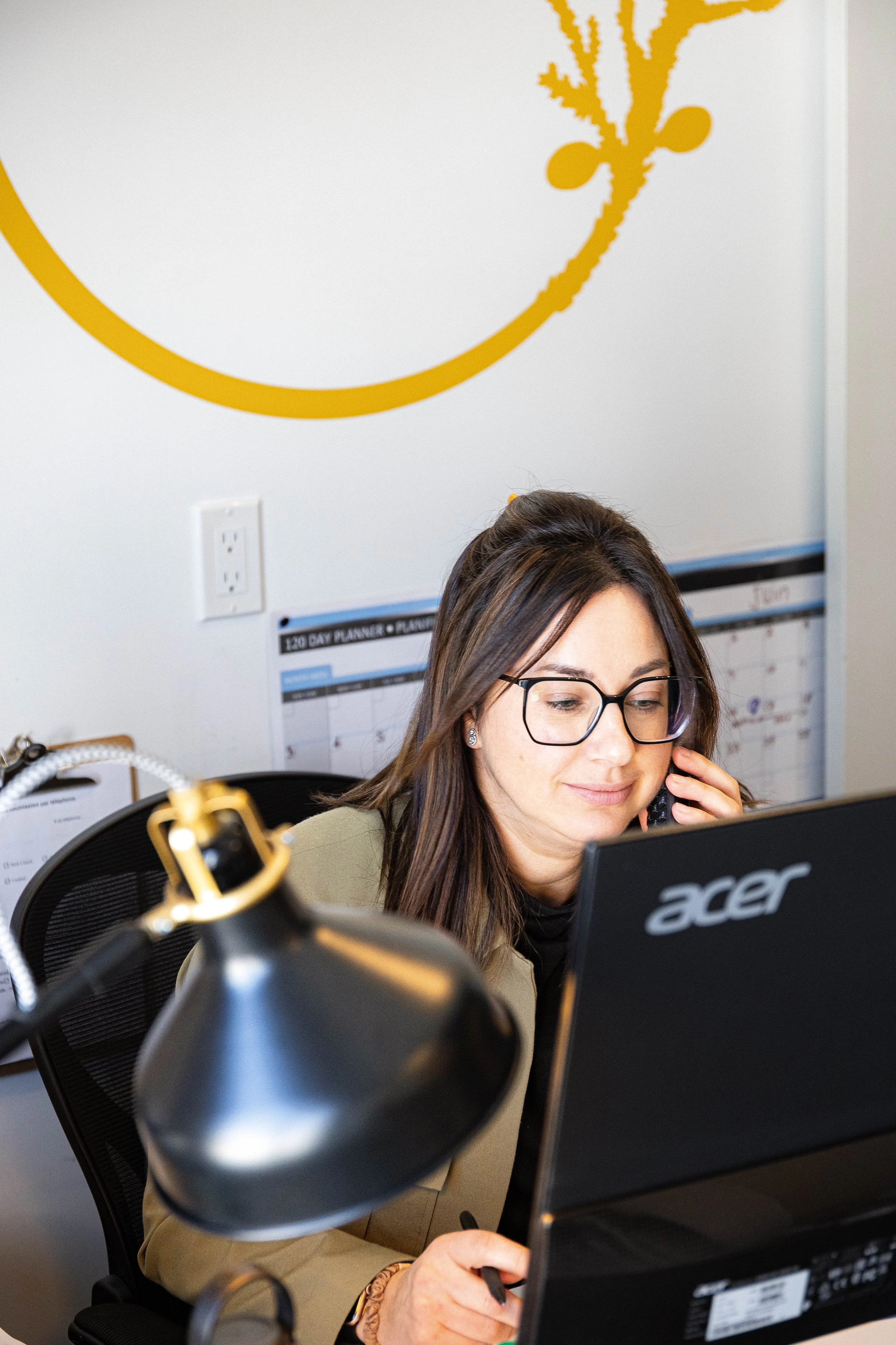 Noémie parle au téléphone tout en travaillant sur un ordinateur portable dans un bureau.