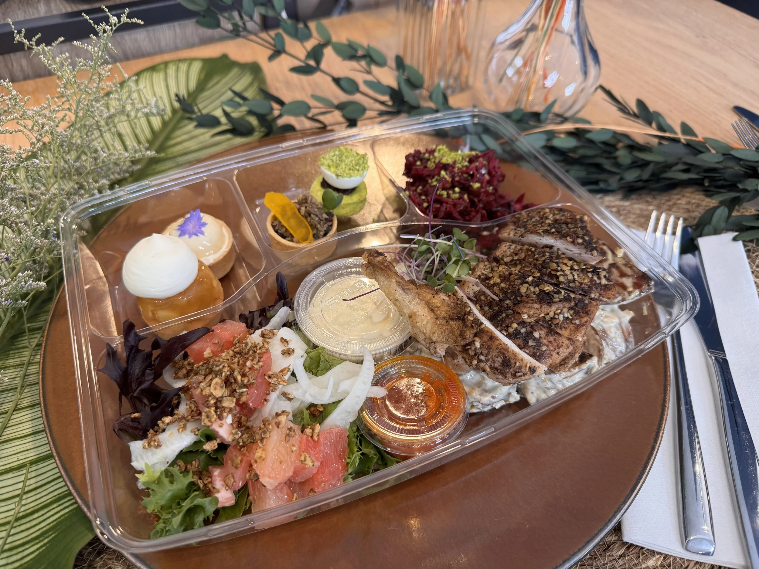 Assiette de nourriture avec salade, poulet, légumes et desserts, sur une table décorée avec des plantes