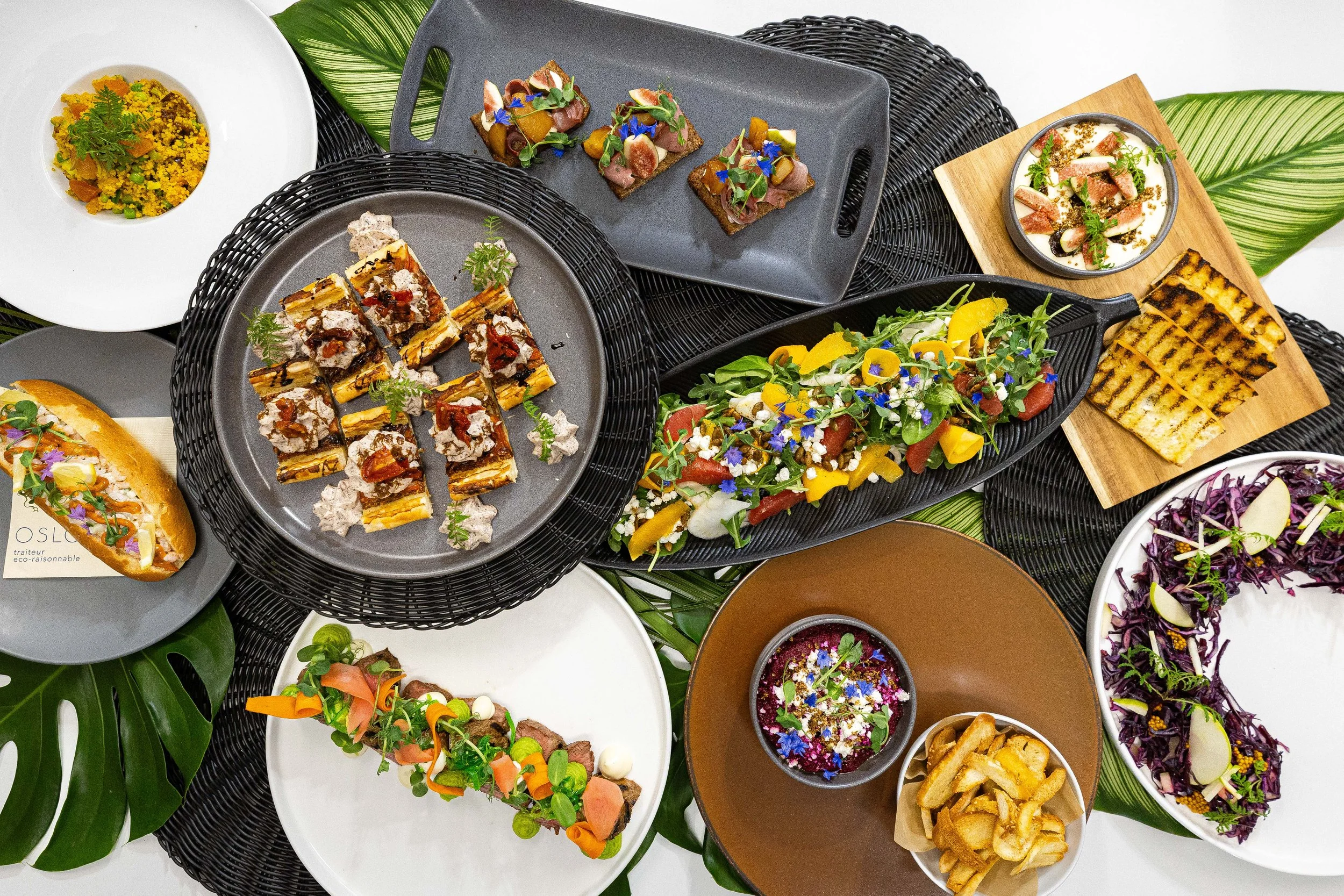 Assortiment de plats colorés et présentation soignée de cuisine végétarienne et végétalienne, y compris des salades, des tartines, des desserts et des accompagnements, décorés de fleurs comestibles et de garnitures fraîches.