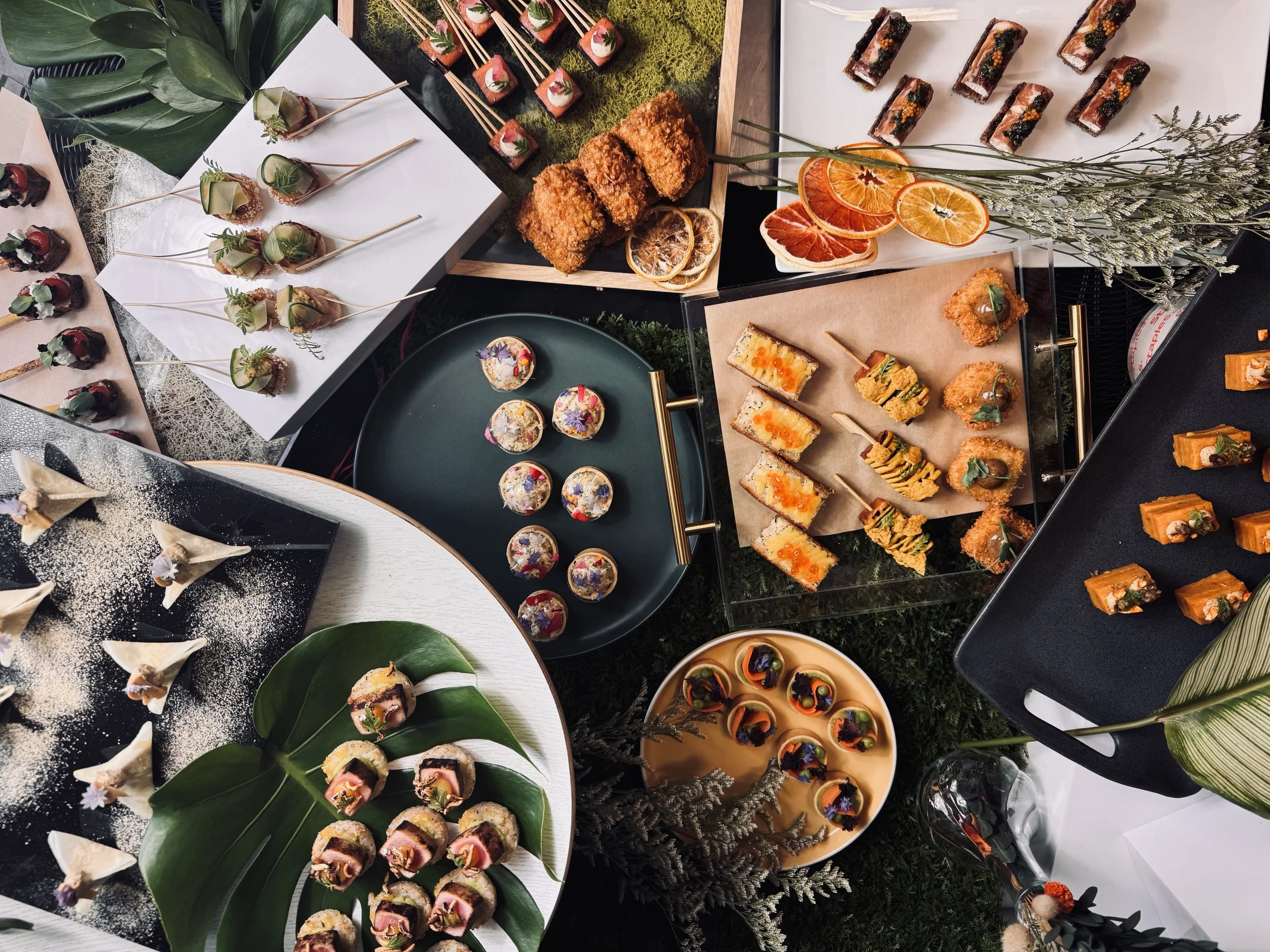 Une variété de petits amuse-gueules et desserts sophistiqués présentés sur des plateaux et des supports décoratifs, avec des fruits et des garnitures colorés.