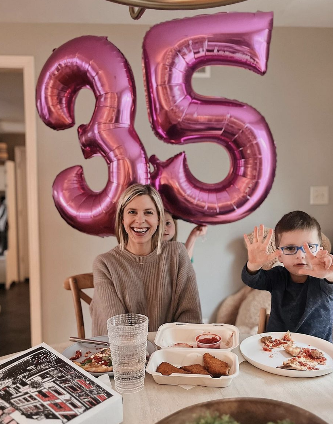 Carly Ritt smiling with balloons in the shape of 35 next to her children