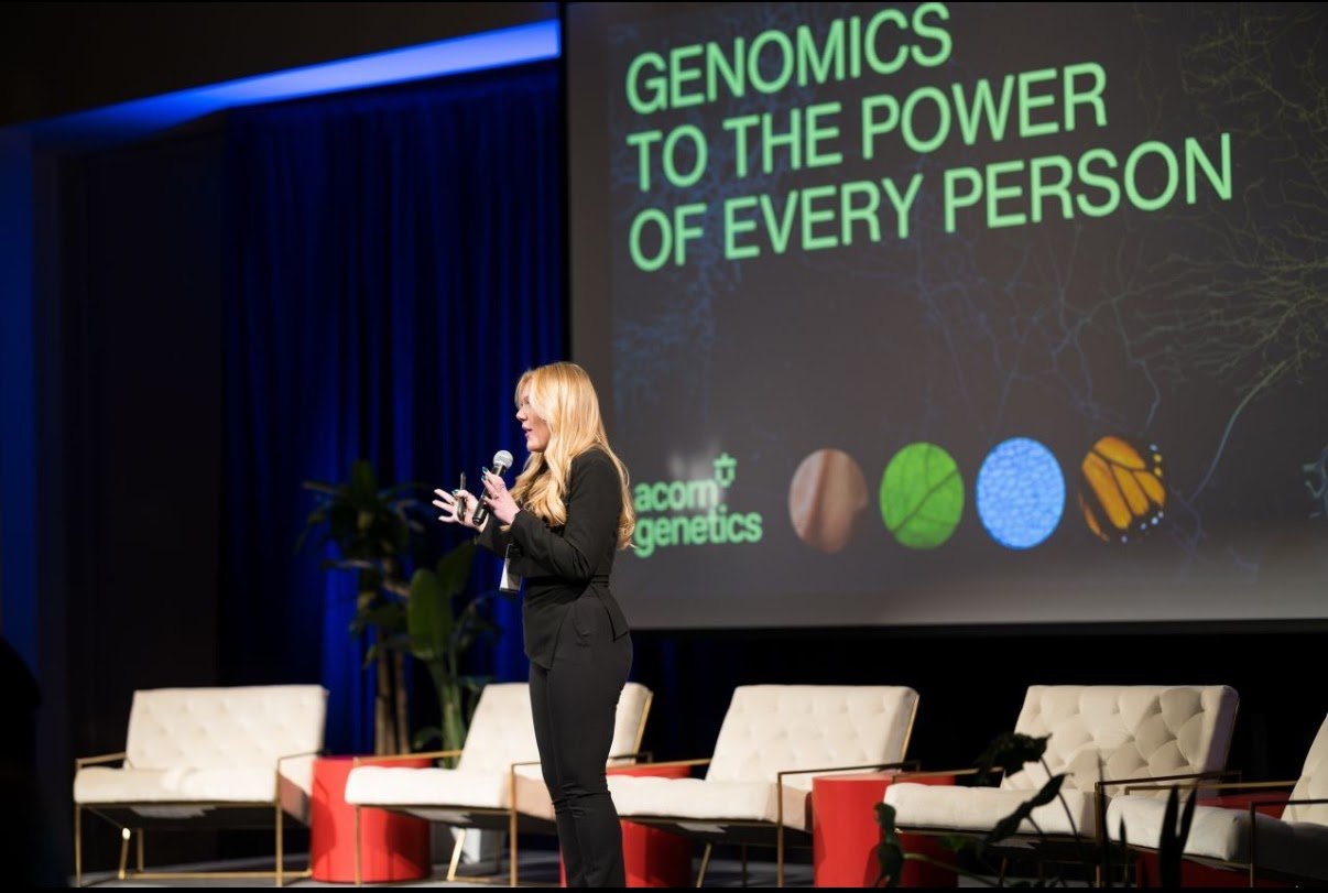 Women on stage giving speech a out Genomics at Noah Liff Opers Center