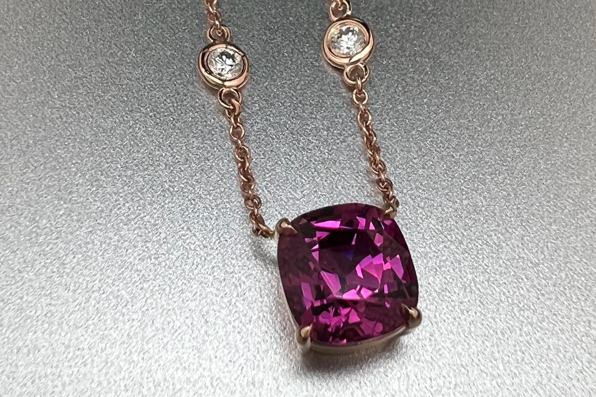 Close-up of a custom 14k rose gold station necklace featuring a 2.28 ct Umbalite garnet with bezel-set natural diamond stations.