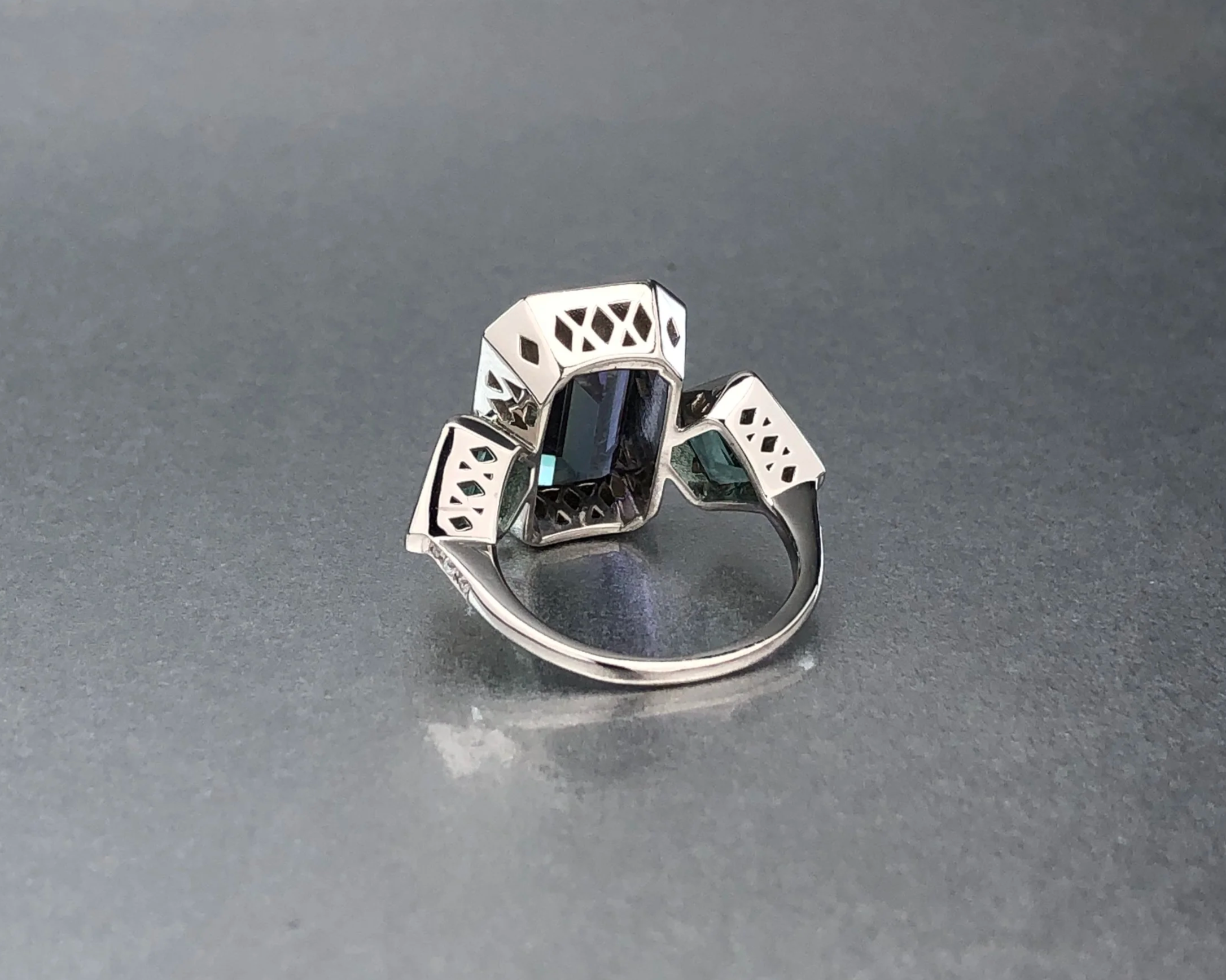 Side view of a custom platinum ring featuring a 4.67 ct emerald-cut tanzanite, matched no-heat kite-shaped lagoon tourmalines, and a natural diamond pavé halo.