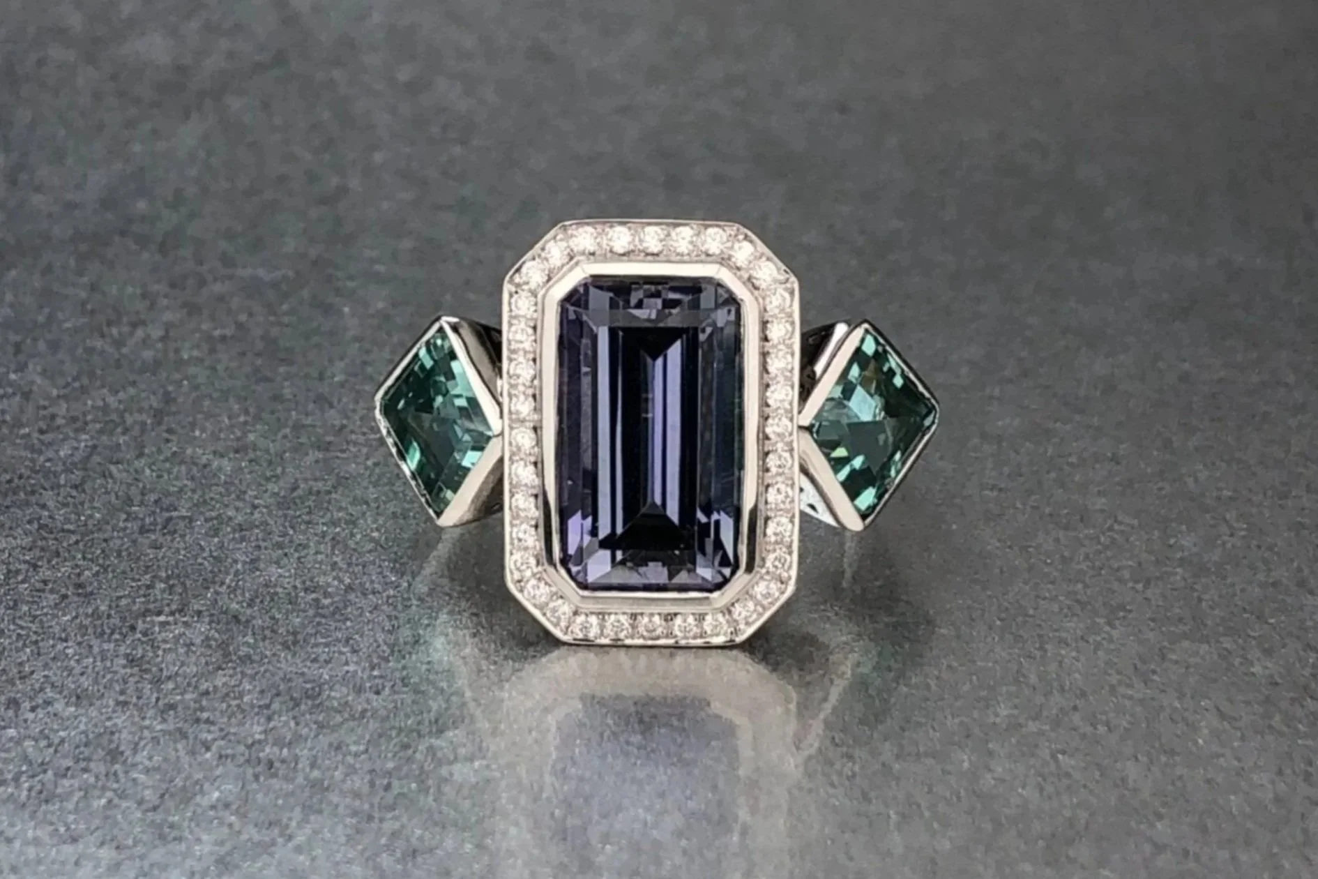 Front view of a custom platinum ring featuring a 4.67 ct emerald-cut tanzanite, matched no-heat kite-shaped lagoon tourmalines, and a natural diamond pavé halo.