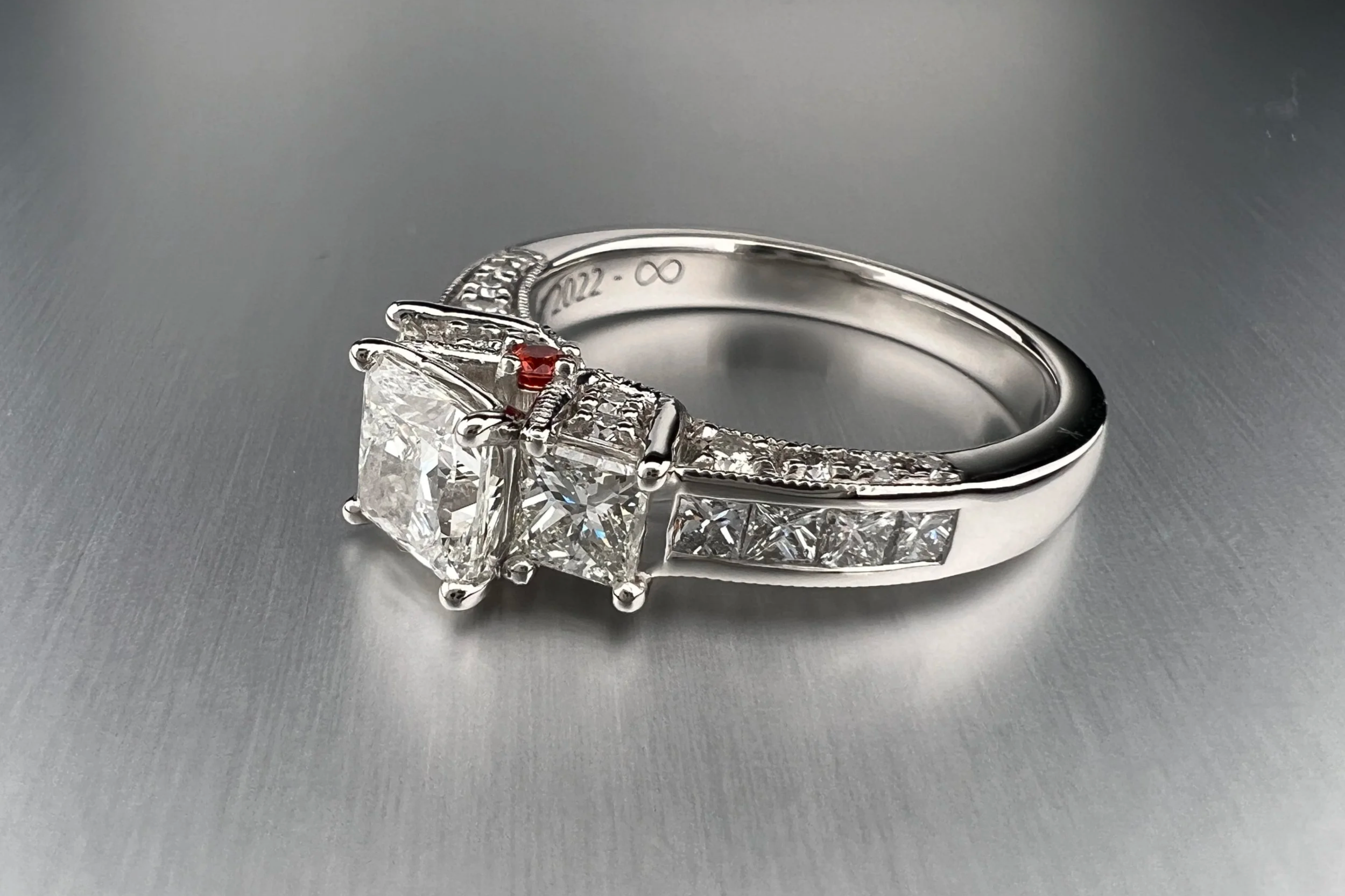 Custom platinum engagement ring featuring a princess-cut natural diamond with tapered natural diamond accents and orange sapphire details.