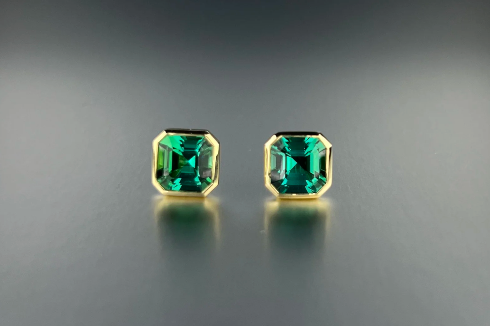 Front view of custom 18k yellow gold bezel-set stud earrings featuring 4.44 tcw no-heat lagoon tourmalines from Brazil.