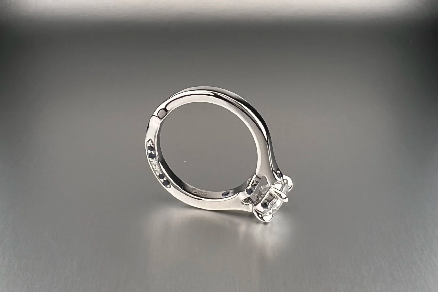 Side view of a custom platinum engagement ring featuring a 1.35 ct Old European cut natural diamond with pavé natural diamonds and blue sapphire accents.