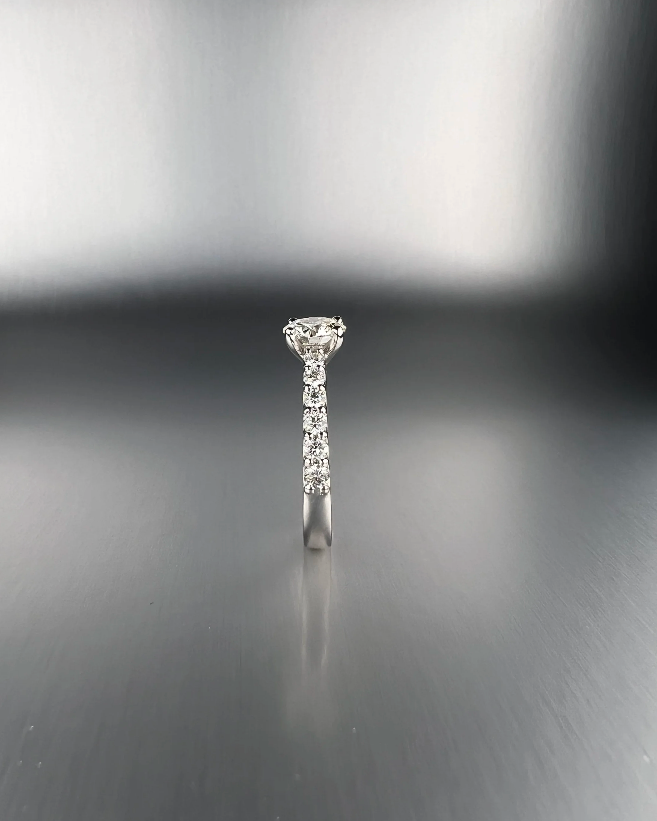 Profile view of a custom platinum engagement ring featuring a 1.00 ct round brilliant natural diamond with pavé natural diamond accents.