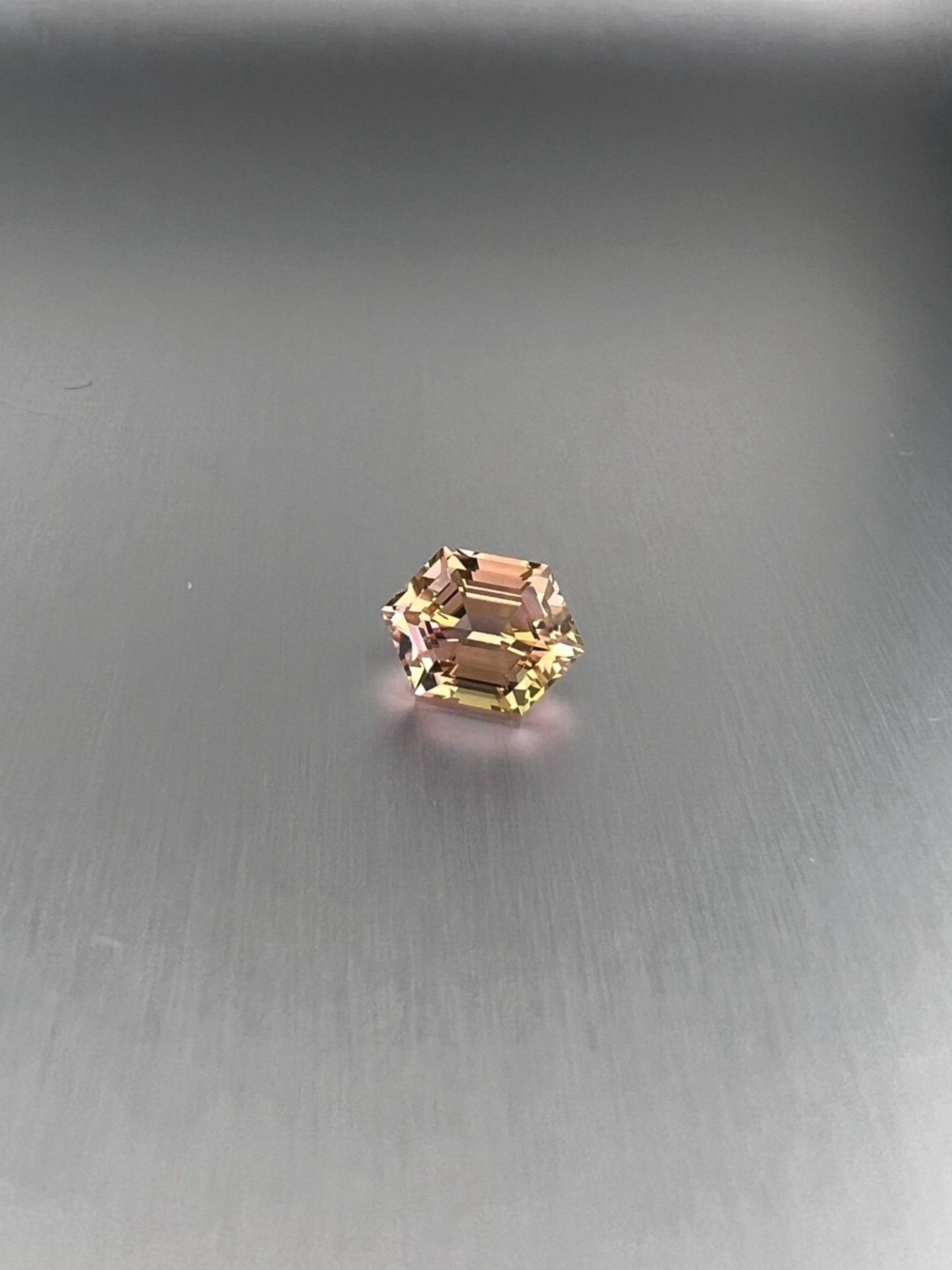 A 2.06 carat bi-color peach tourmaline with a hexagon cut, displaying stunning peach hues and exceptional clarity, highlighting its unique and elegant gem quality.