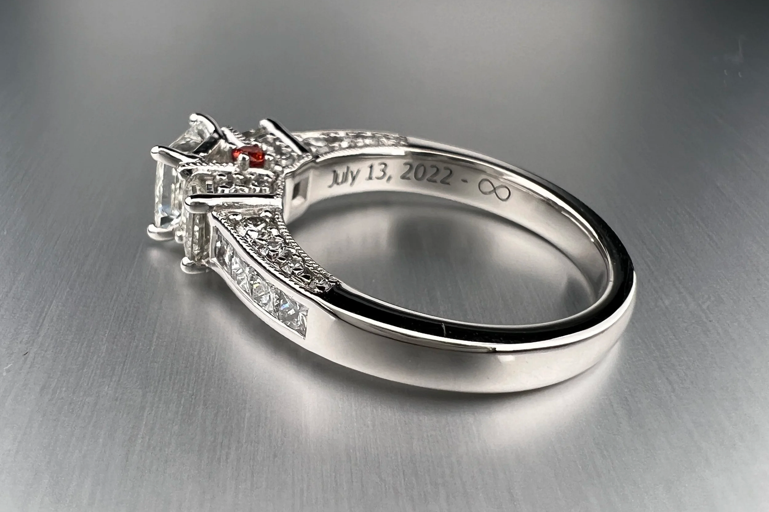 Front view of a custom platinum engagement ring featuring a princess-cut natural diamond with tapered natural diamond accents and orange sapphire details.