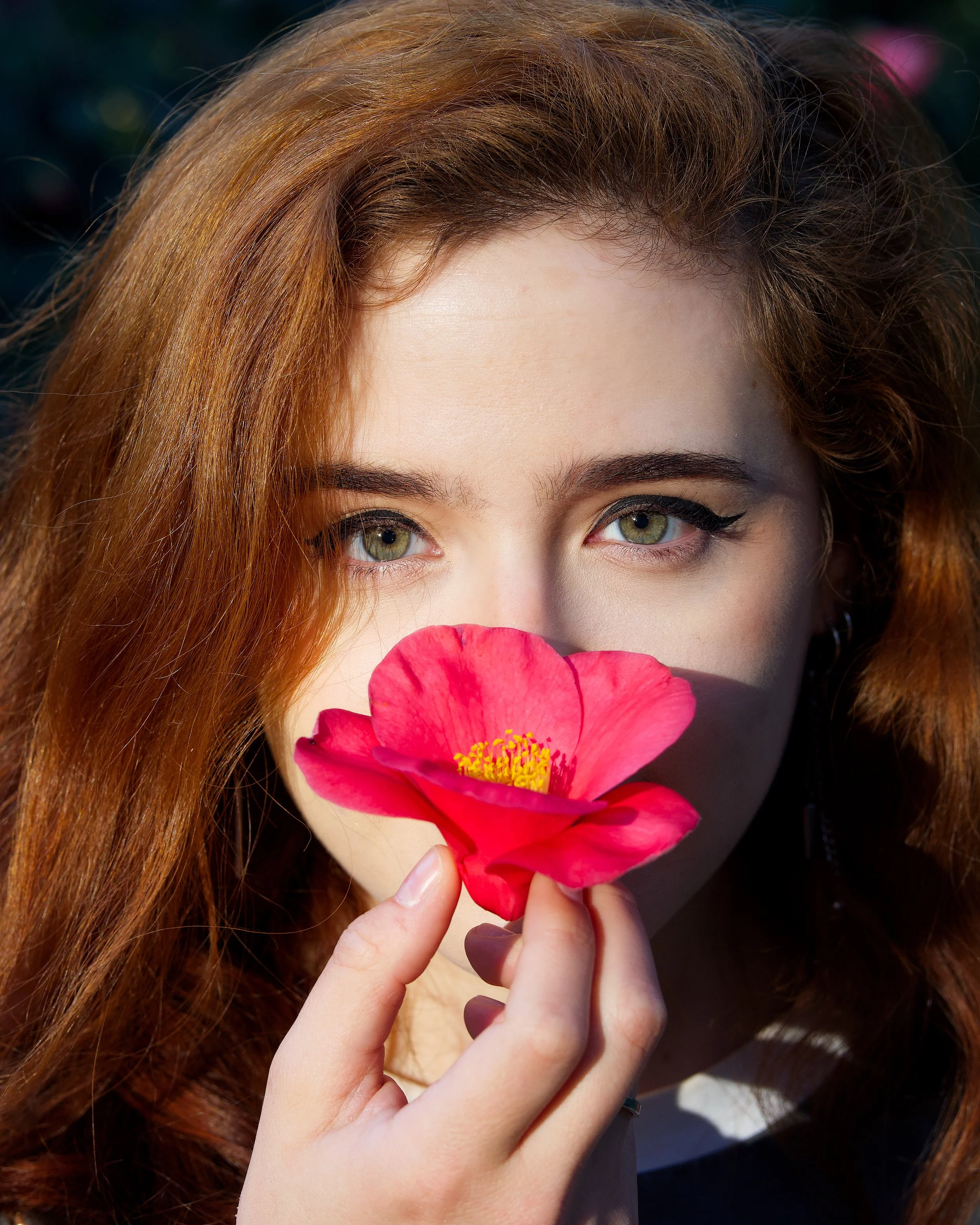 Close-up editorial headshot of actress Tatyana Aravena holding a pink camellia blossom in natural light during a NYC creative portrait session.