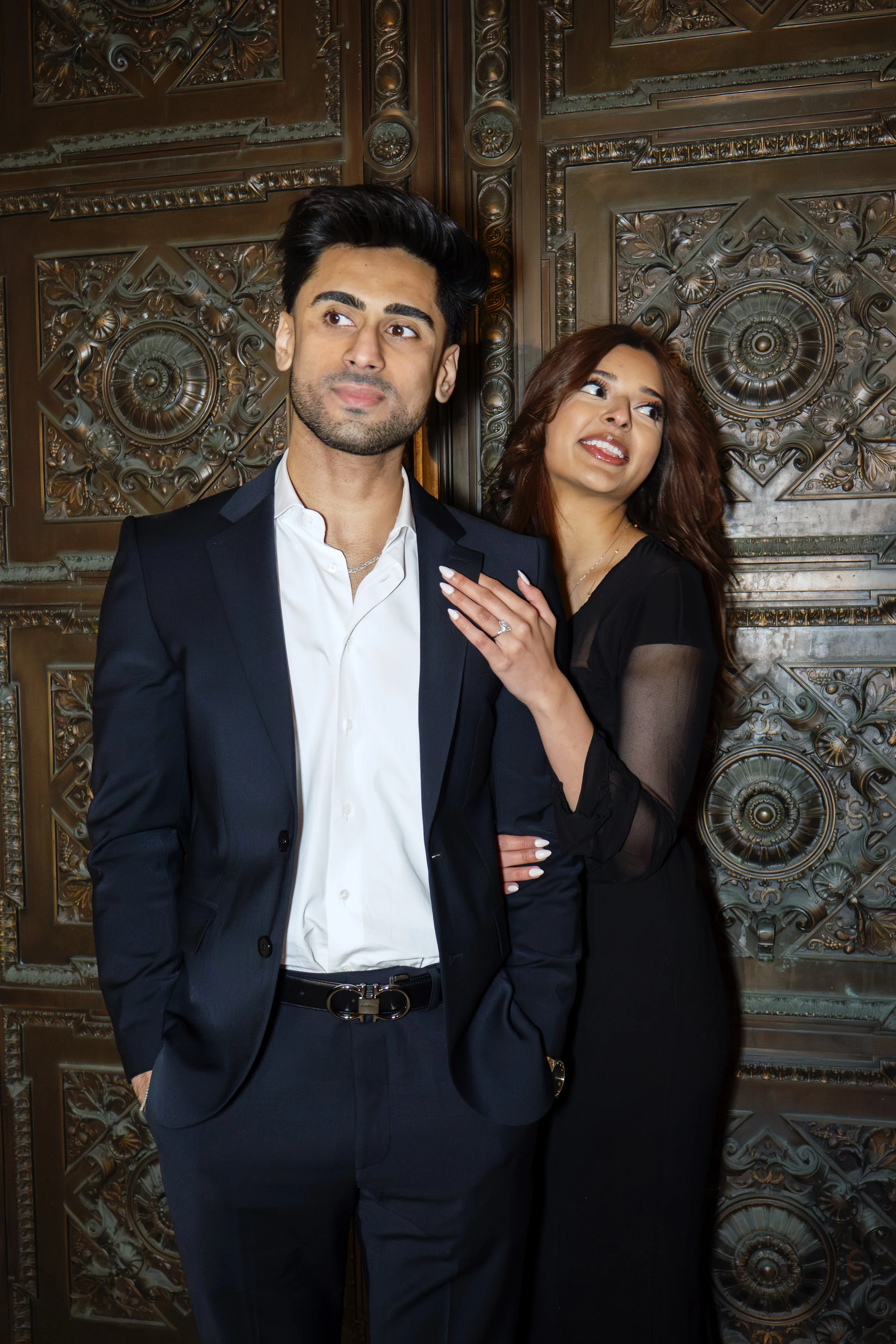 Elegantly dressed couple in formal wear posed against ornate carved architectural doors during an urban NYC lifestyle portrait session/ stylish outdoor photographer for portrait session/editorial couple poses NYC