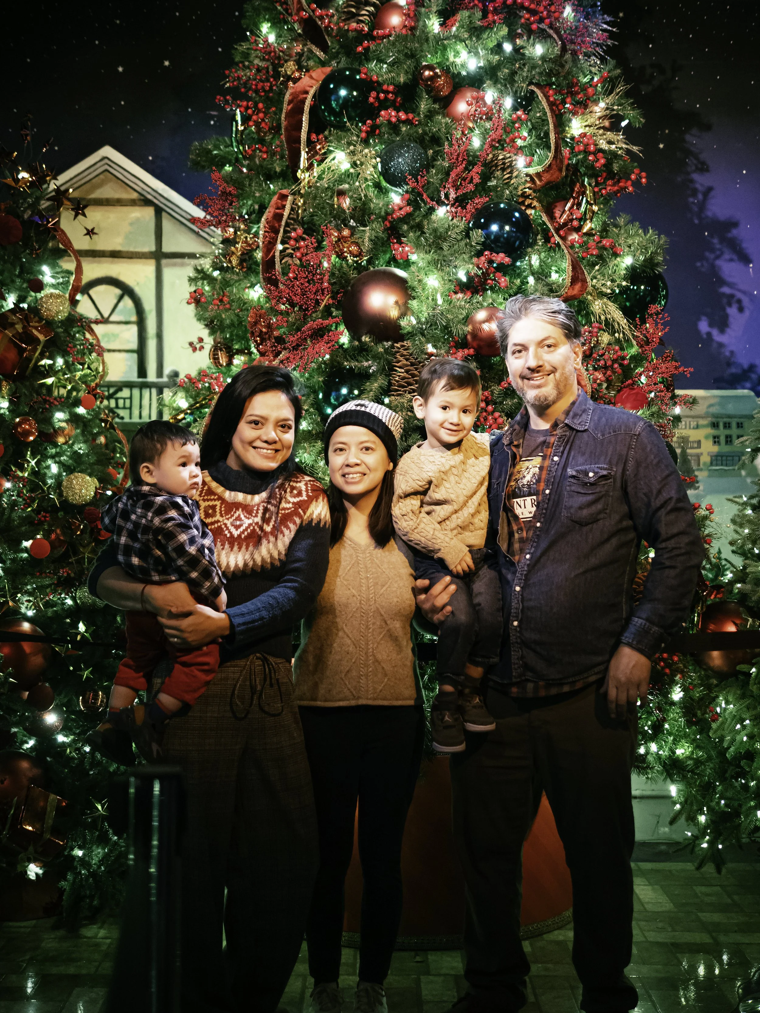 Family posing for a holiday portrait in front of a decorated Christmas tree during a NYC family photo session