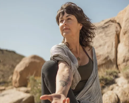 Woman practicing yoga outdoors in a rocky desert landscape.