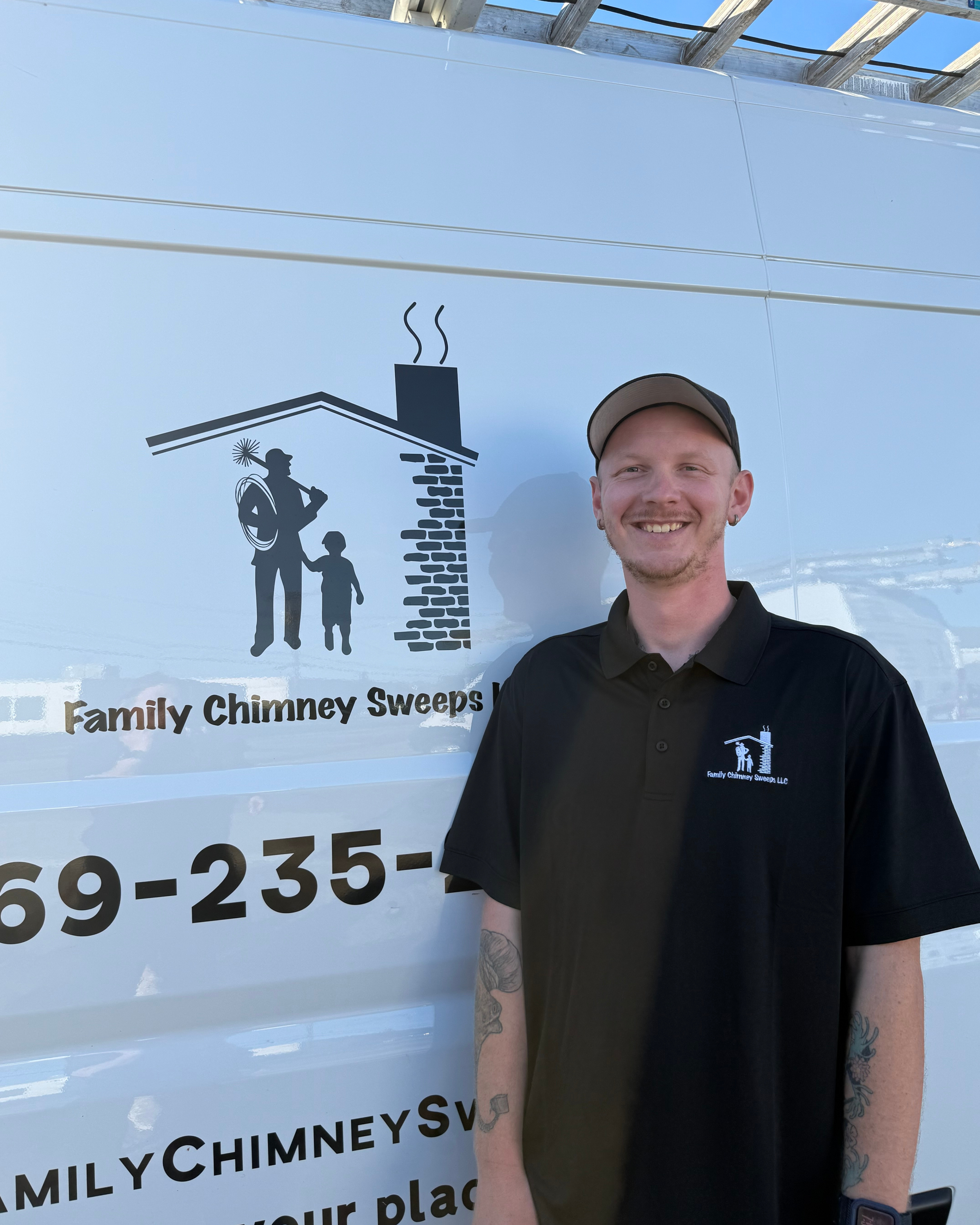 A man in a black polo shirt with a Family Chimney Sweeps LLC logo stands outdoors in front of a white van with the same logo, smiling at the camera.