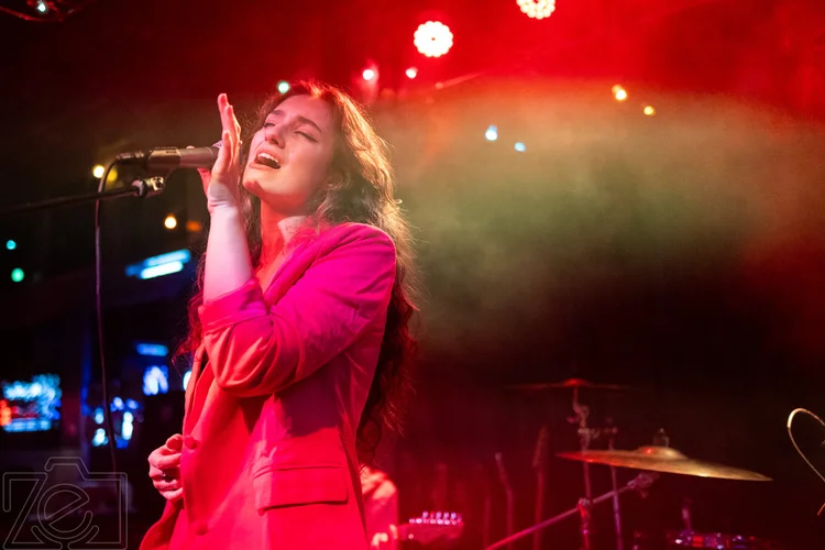 Singer in a hot pink blazer performing under red stage light