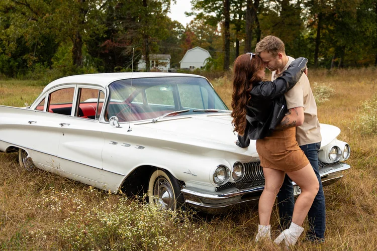 Couple embracing beside a vintage white Buick in an autumn field