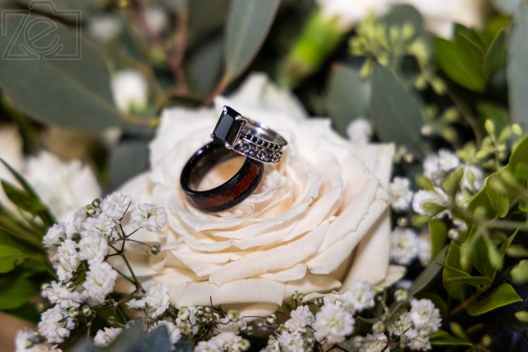 Wedding rings resting on a cream rose with baby's breath and eucalyptus