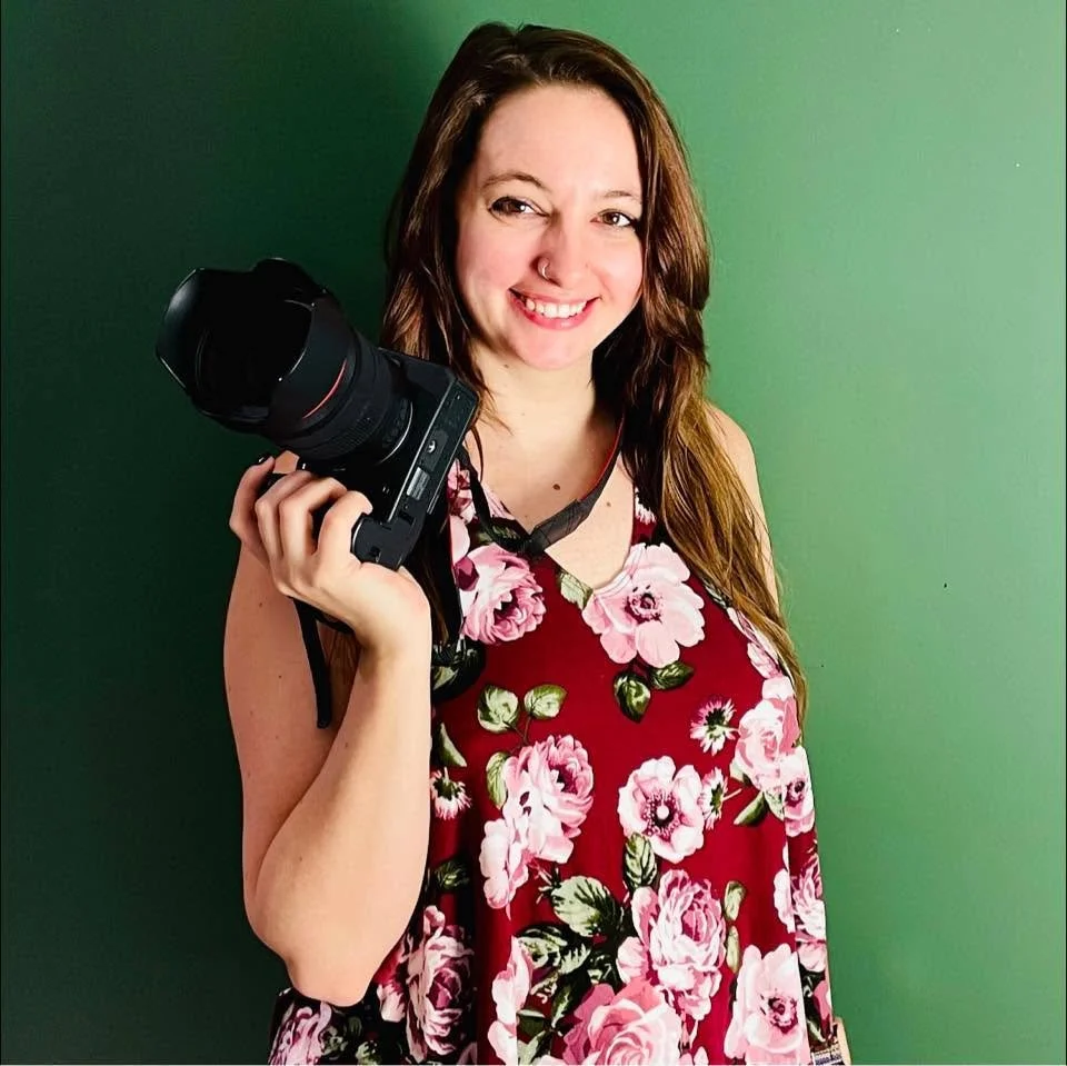 Zoe in a floral sleeveless dress holding a camera against a green background