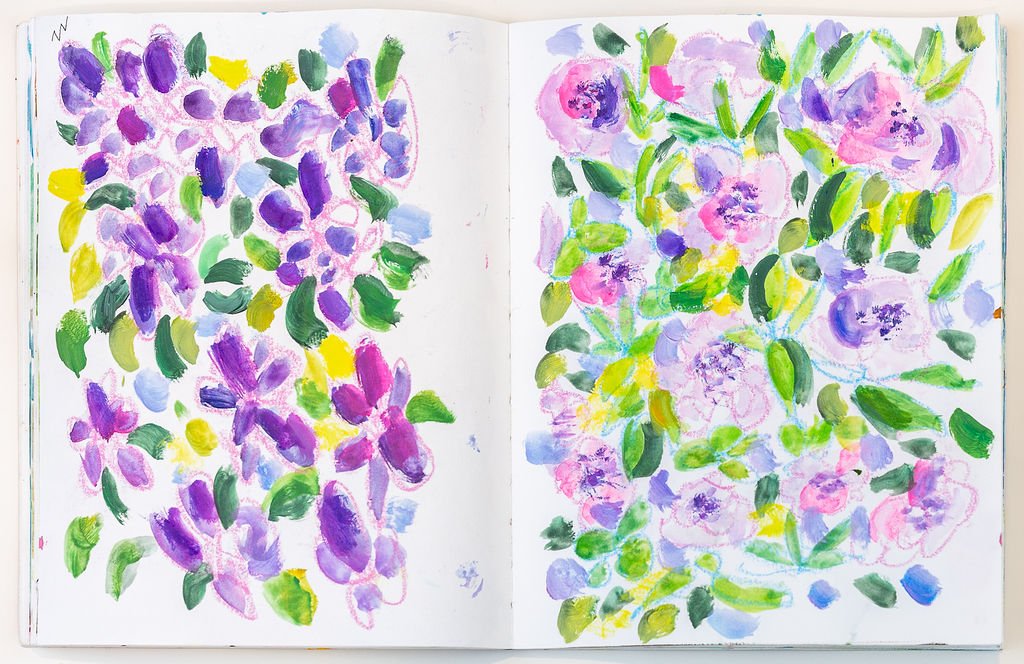 A watercolor painting of assorted purple, pink, and yellow flowers with green leaves on a white background. The flowers are scattered across the pages of a sketchbook.