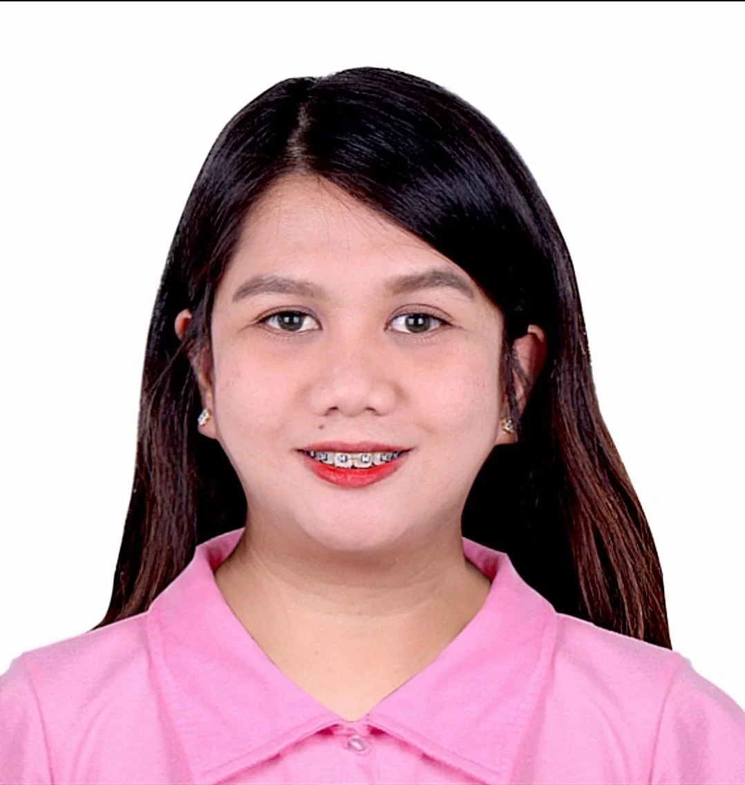 A young woman with straight reddish-brown hair smiling, wearing a bright pink blouse and small earrings, against a plain white background.
