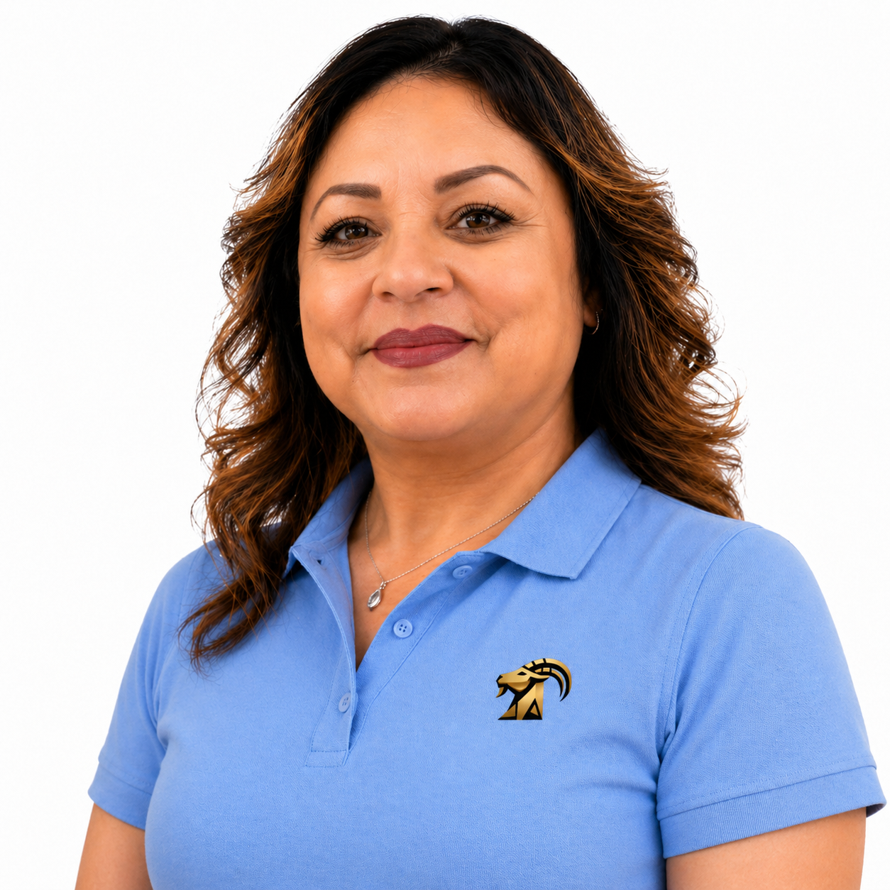 A woman with long brown hair wearing a blue collared shirt with a yellow and blue lion logo, smiling, standing against a plain white wall.