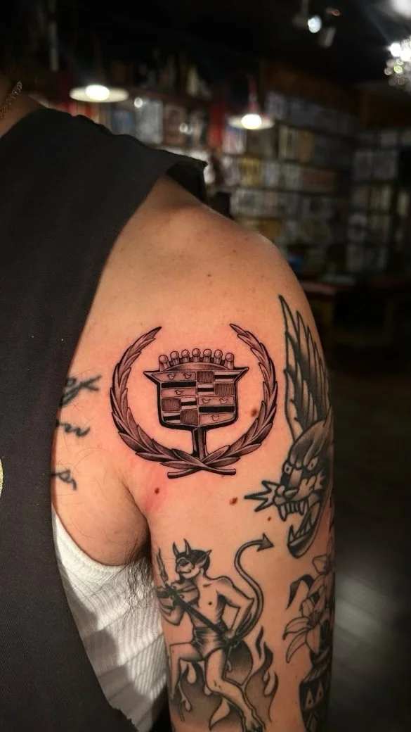 Black and gray emblem tattoo on the shoulder by Lexi at Electric Street Tattoo, Fort Lauderdale