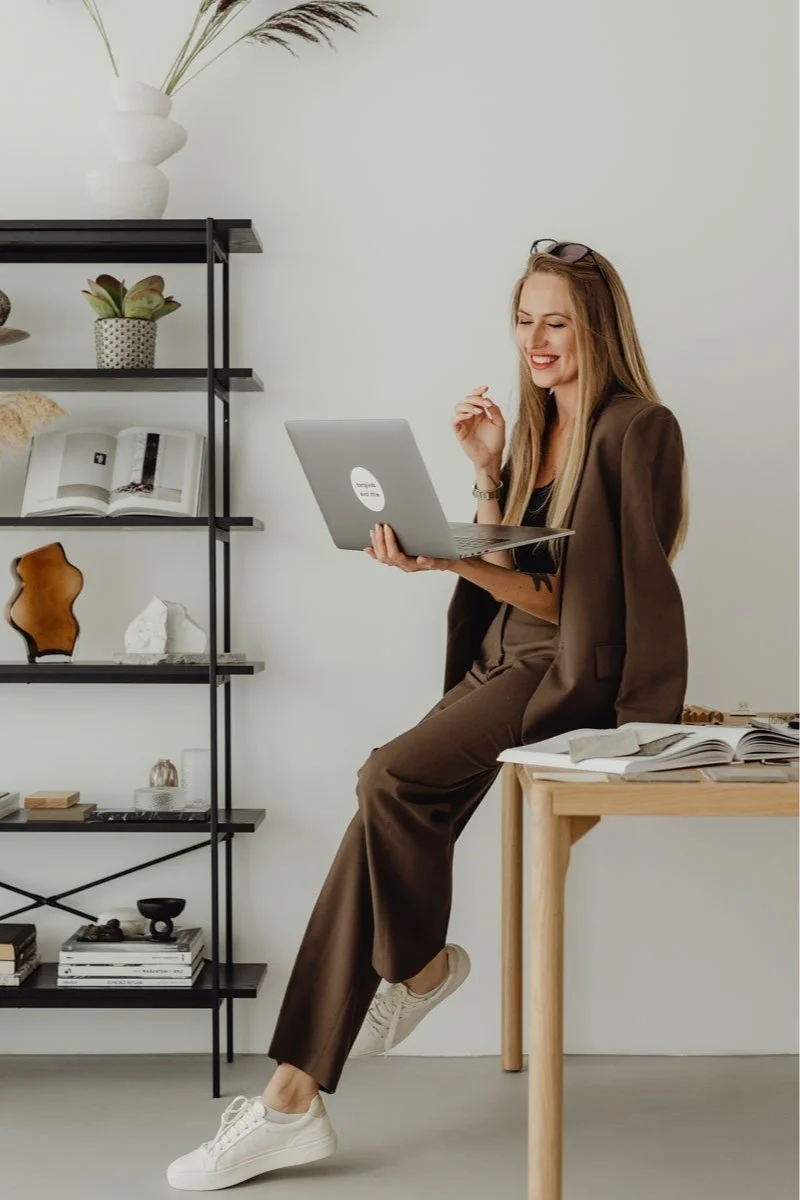 Female interior designer sitting on desk using laptop with decorative bookshelves behind
