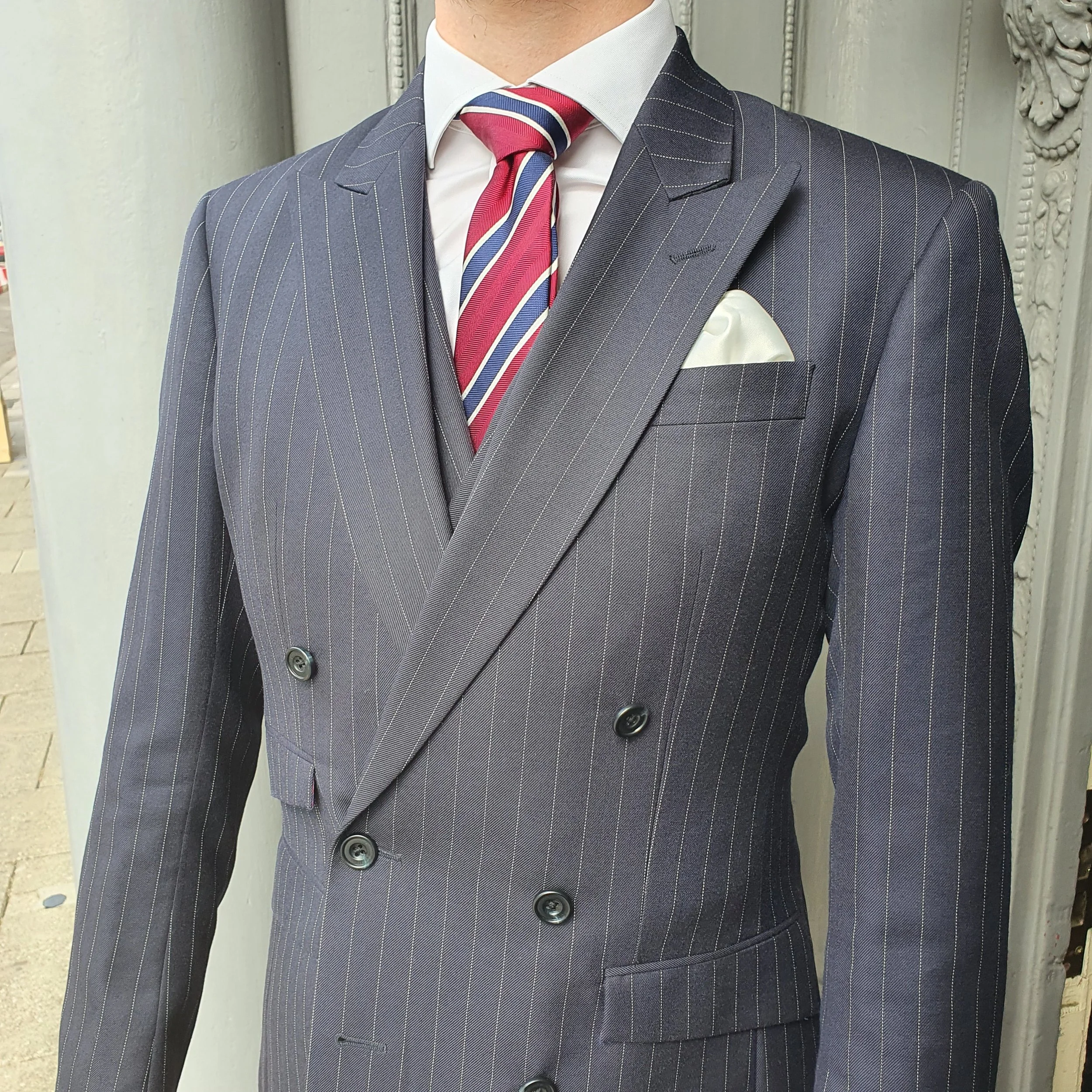 Close-up of a mannequin dressed in a navy pinstripe double-breasted suit, white shirt, red, white, and blue striped tie, and a white pocket square.