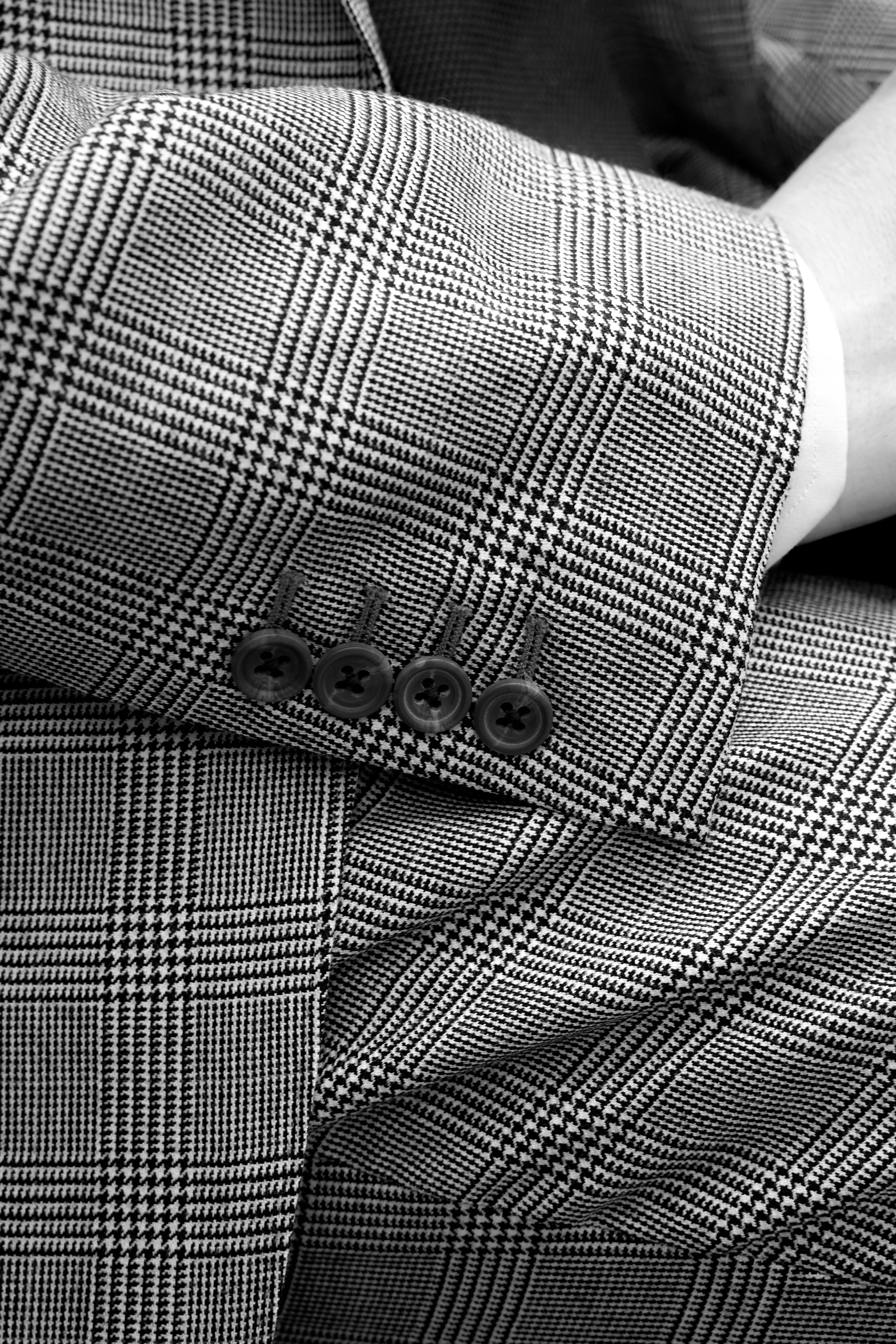 Close-up of a person's arm in a checkered patterned blazer with four buttons on the sleeve, with a white shirt visible underneath.
