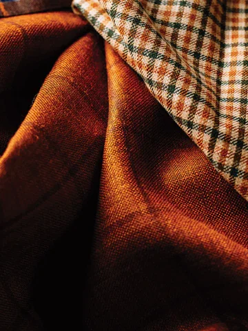Close-up of a fabric with an orange and brown plaid pattern on top of a textured brown cloth.