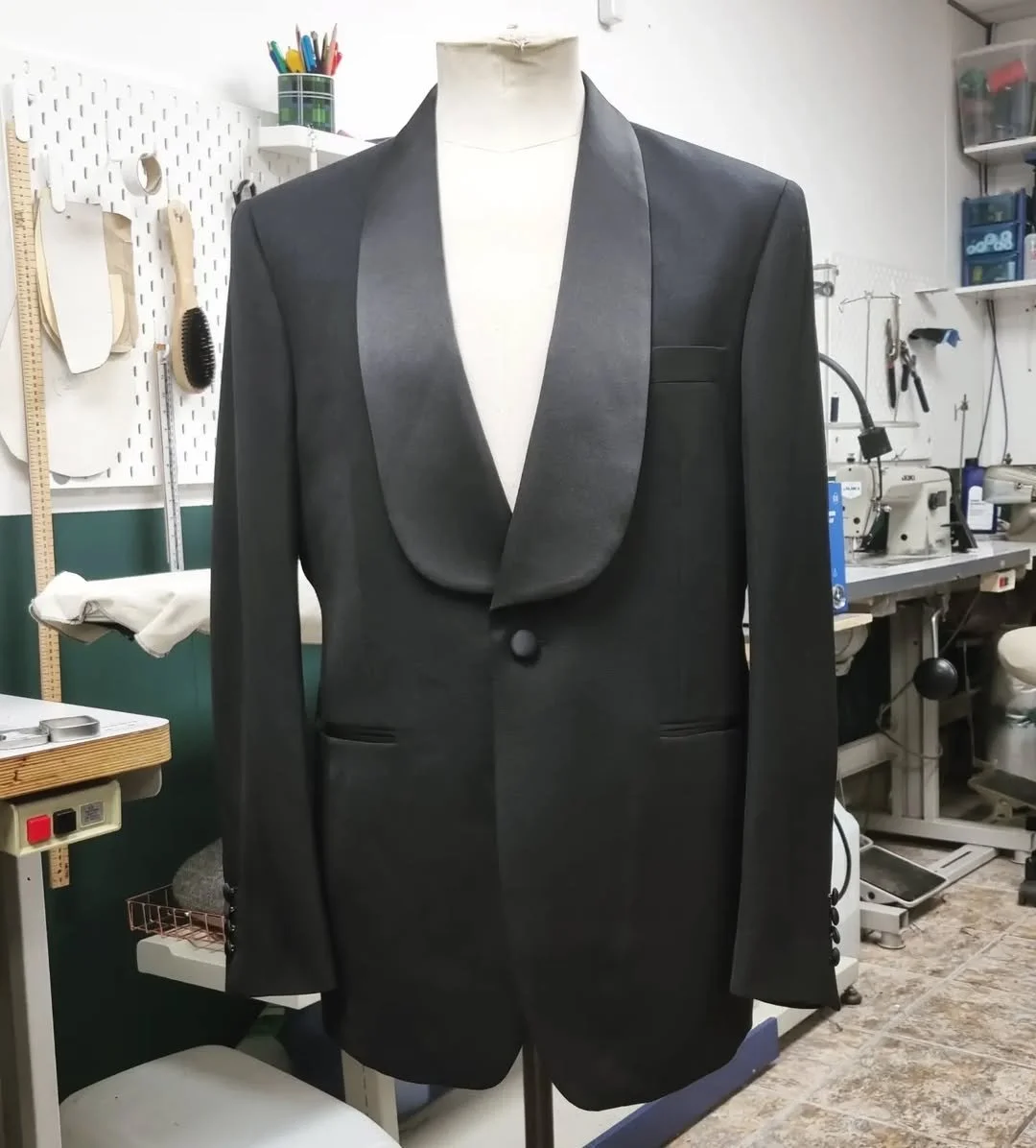 A black tuxedo jacket with satin lapels on a dress form in a tailoring workshop.