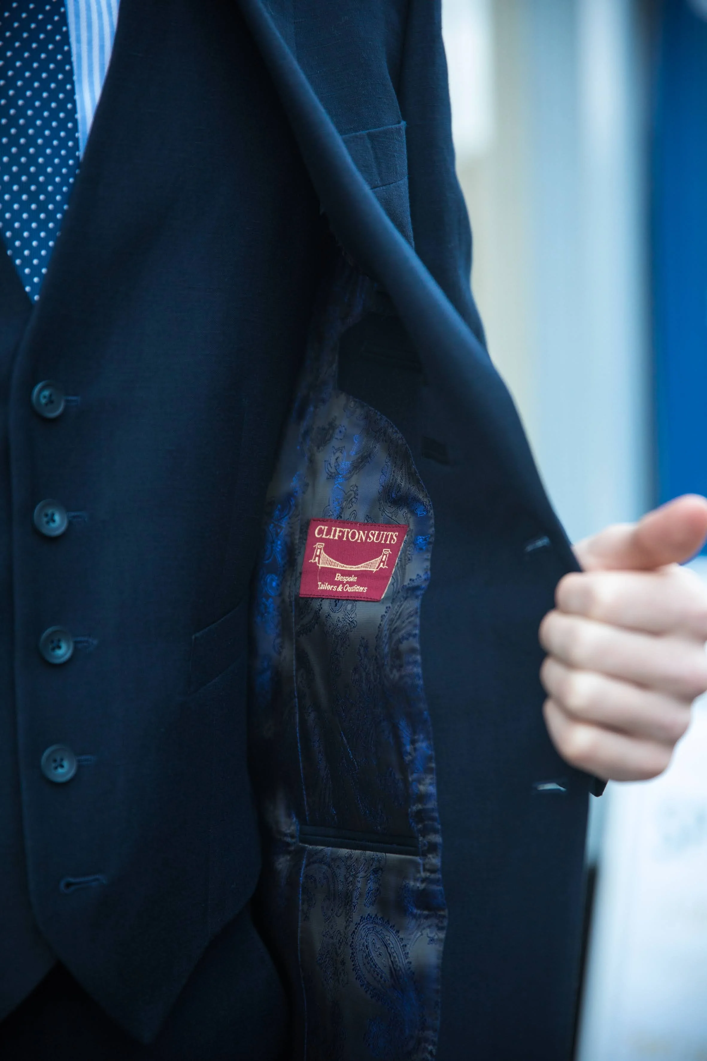 Person displaying the inside lining of a suit jacket showing a "Clifton Suits" label.