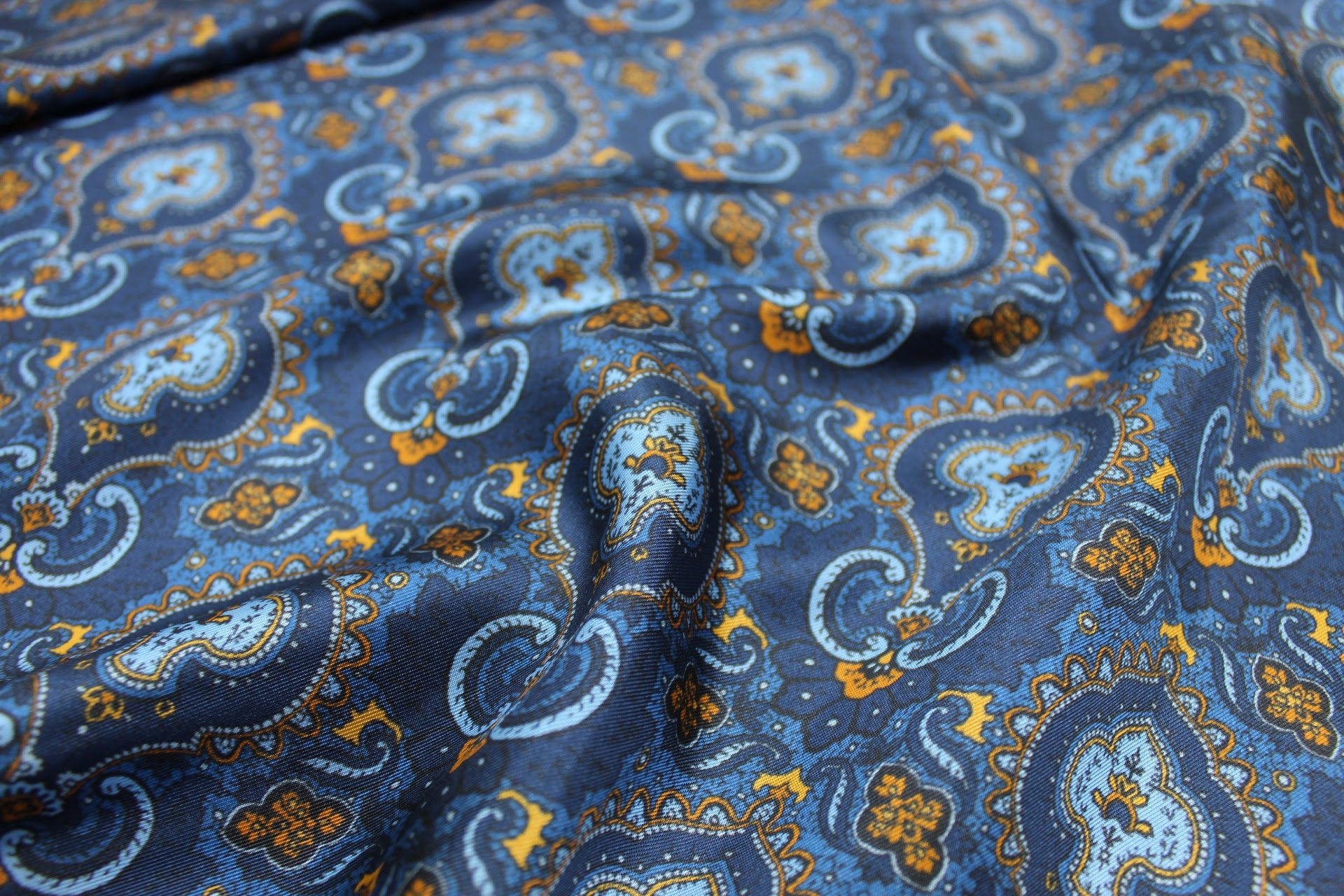 Close-up of blue fabric with a paisley pattern in light blue, orange, and yellow colors.
