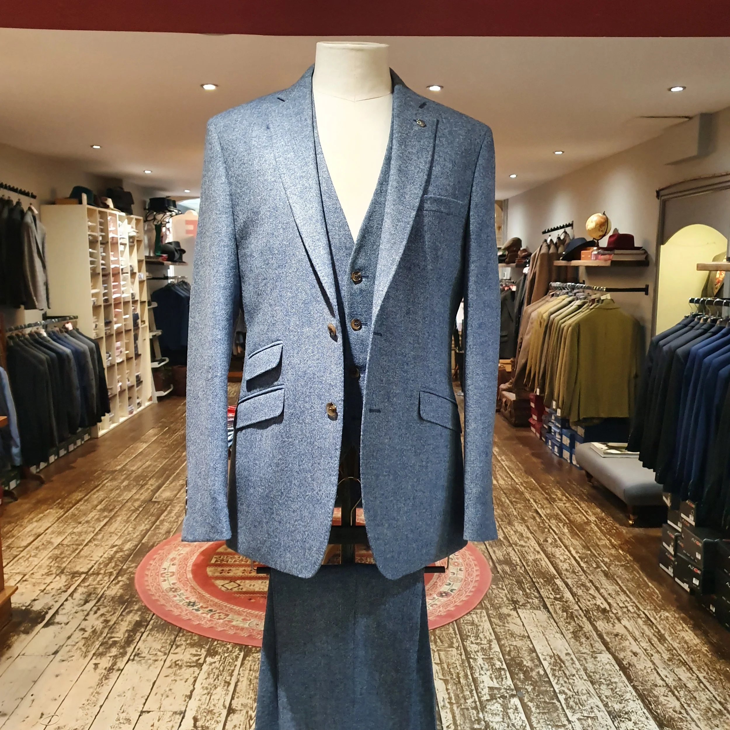 Blue men's suit jacket on a mannequin in a clothing store, with shirts and jackets on racks in the background.