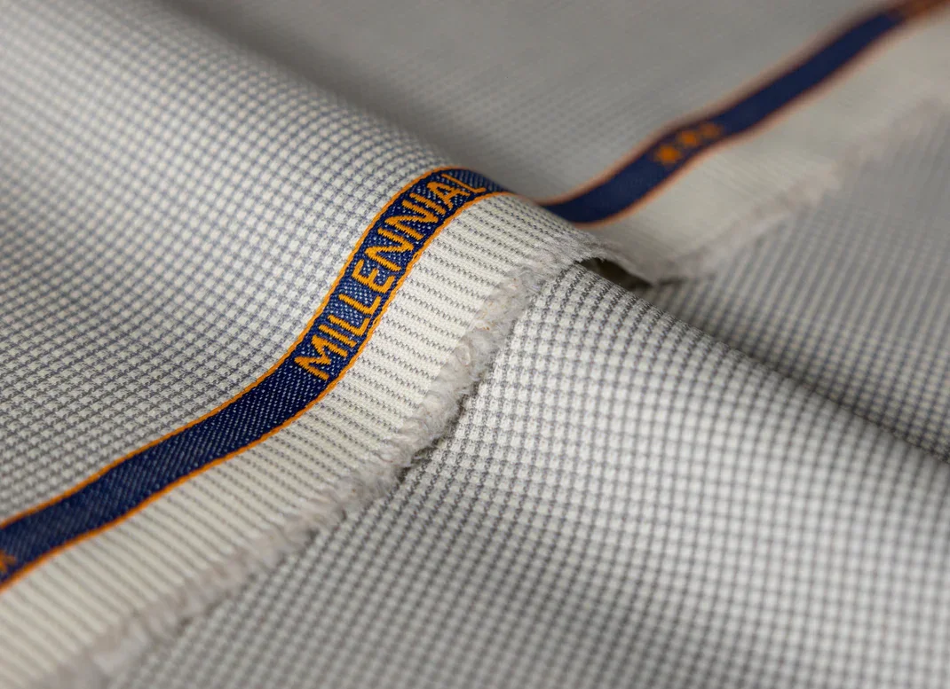 Close-up of a light-colored, checkered dress shirt with a brand tag that reads 'MILLEFILIENNA' and dark blue and orange piping along the seams.