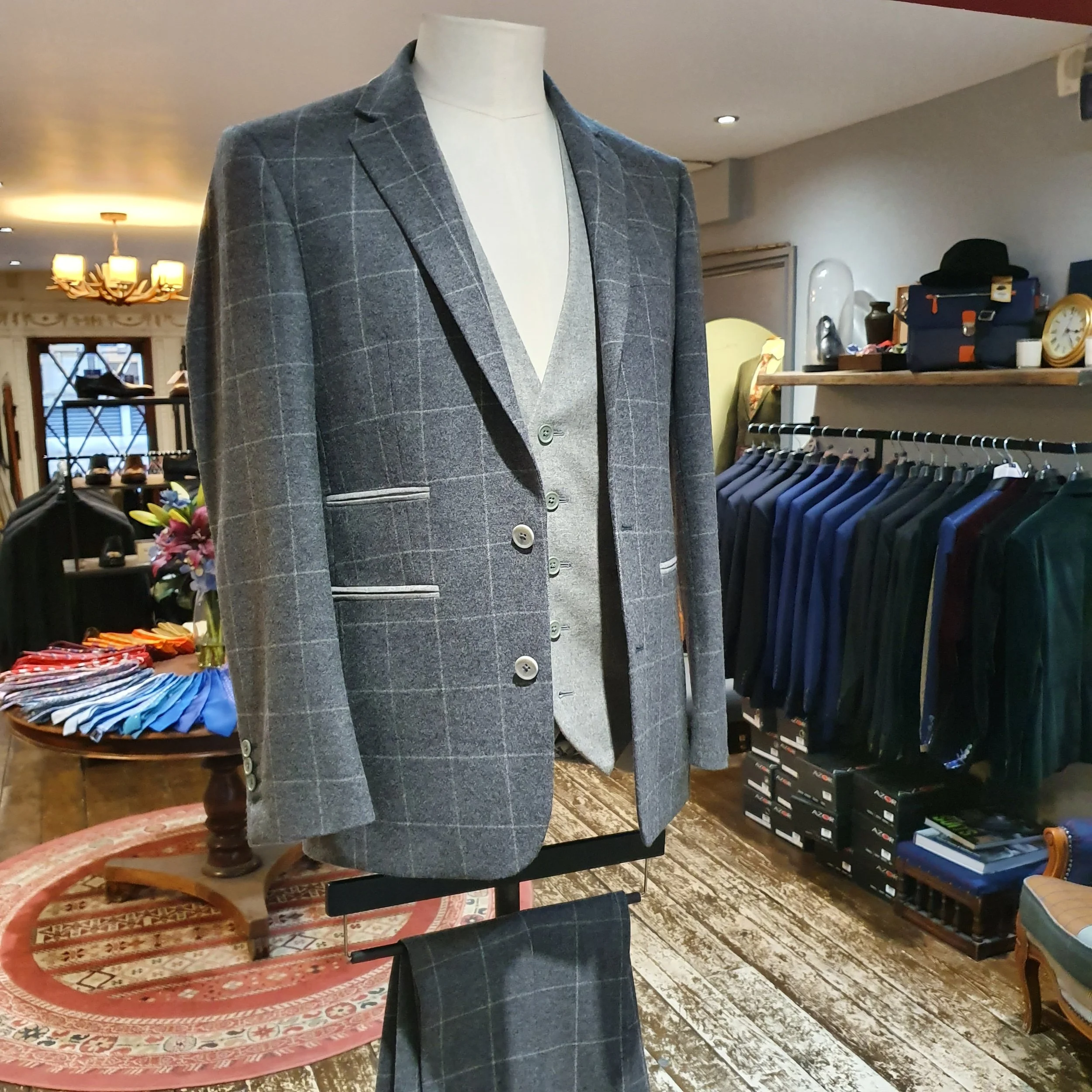 Mannequin wearing a grey plaid blazer over a grey vest and white shirt inside clothing store.