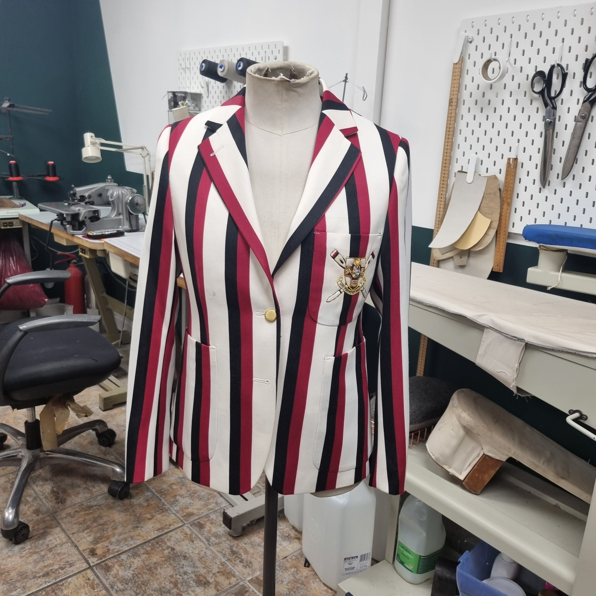 A striped blazer with red, black, and white vertical stripes displayed on a mannequin in a tailoring or sewing workshop.