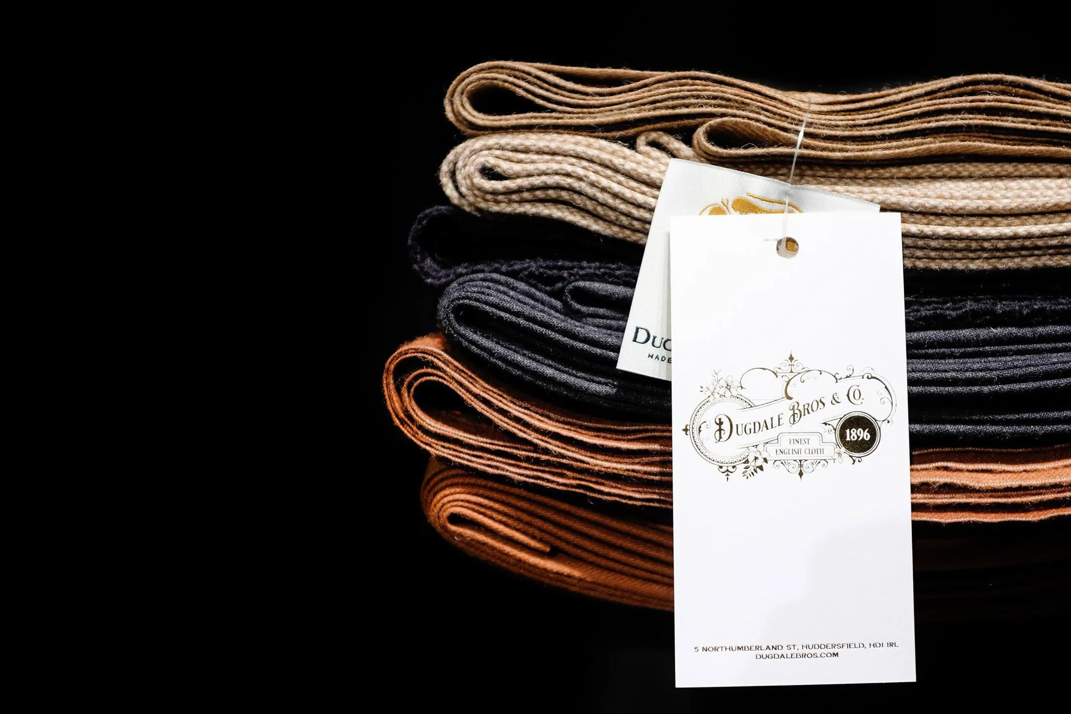 Stacked assorted colored socks with a Dugdale Bros & Co. tag hanging from the top sock, against a black background.