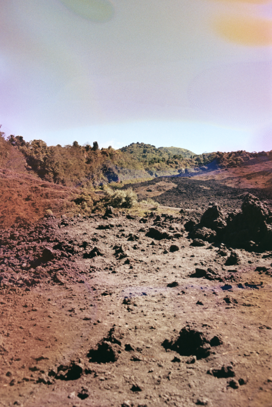 A barren, rocky mountain landscape with sparse vegetation and hills in the background under a clear sky.