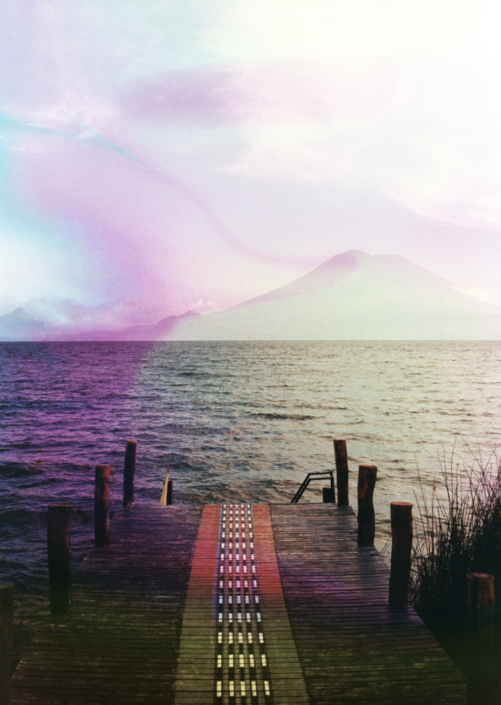 A dock extends into a body of water with mountains and a volcano in the background, overlaid with pastel-colored clouds and light streaks.
