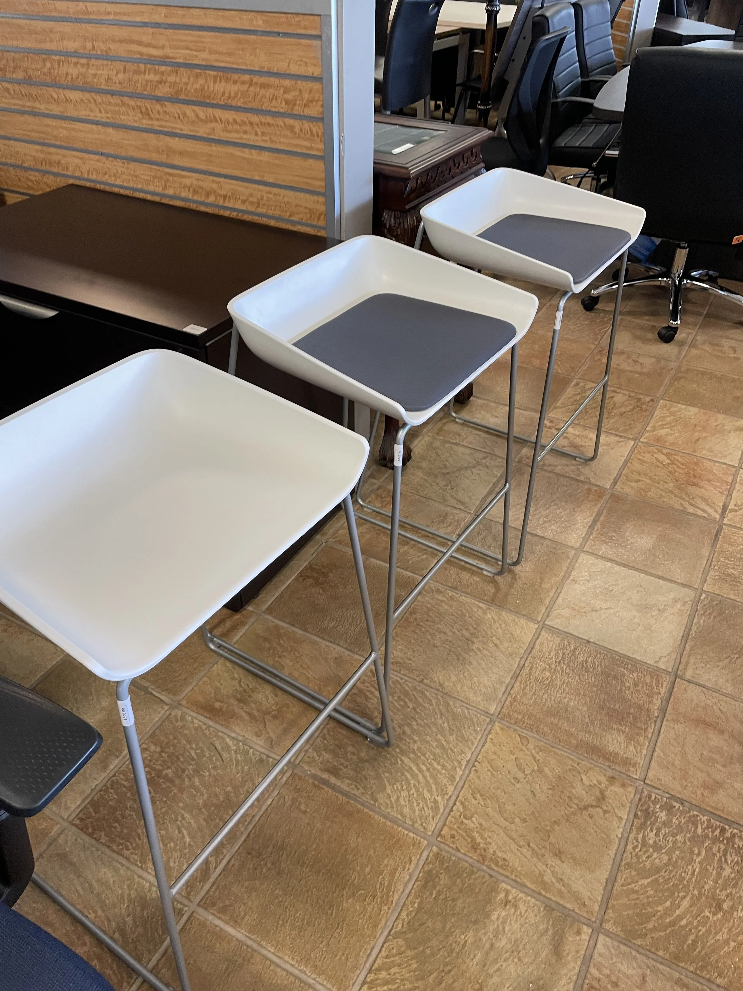 Set of three modern white trays with gray surfaces on metal stands, positioned on a tiled floor in an indoor furniture store.