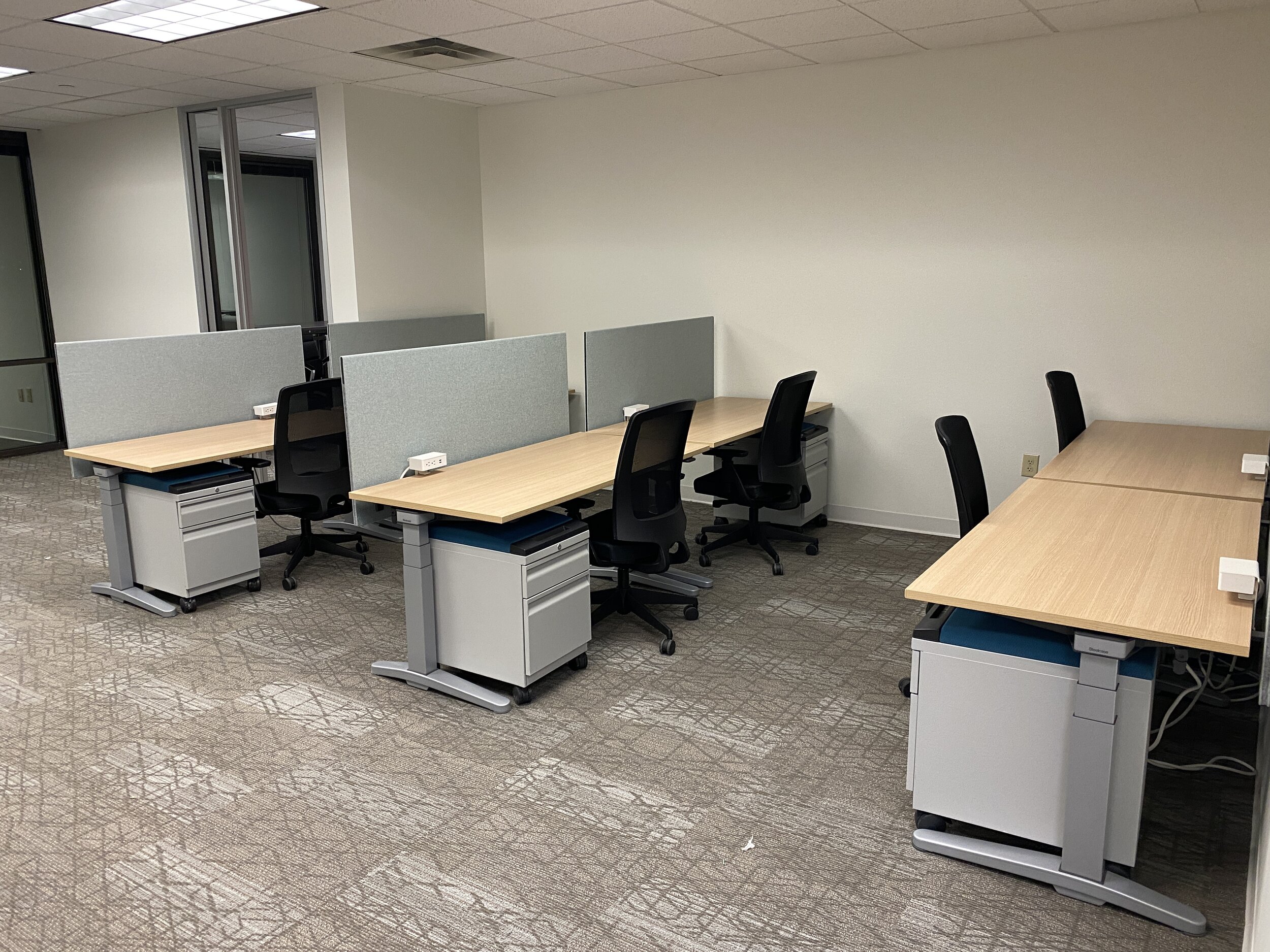 Empty office cubicles with desks, chairs, and power outlets on a carpeted floor.