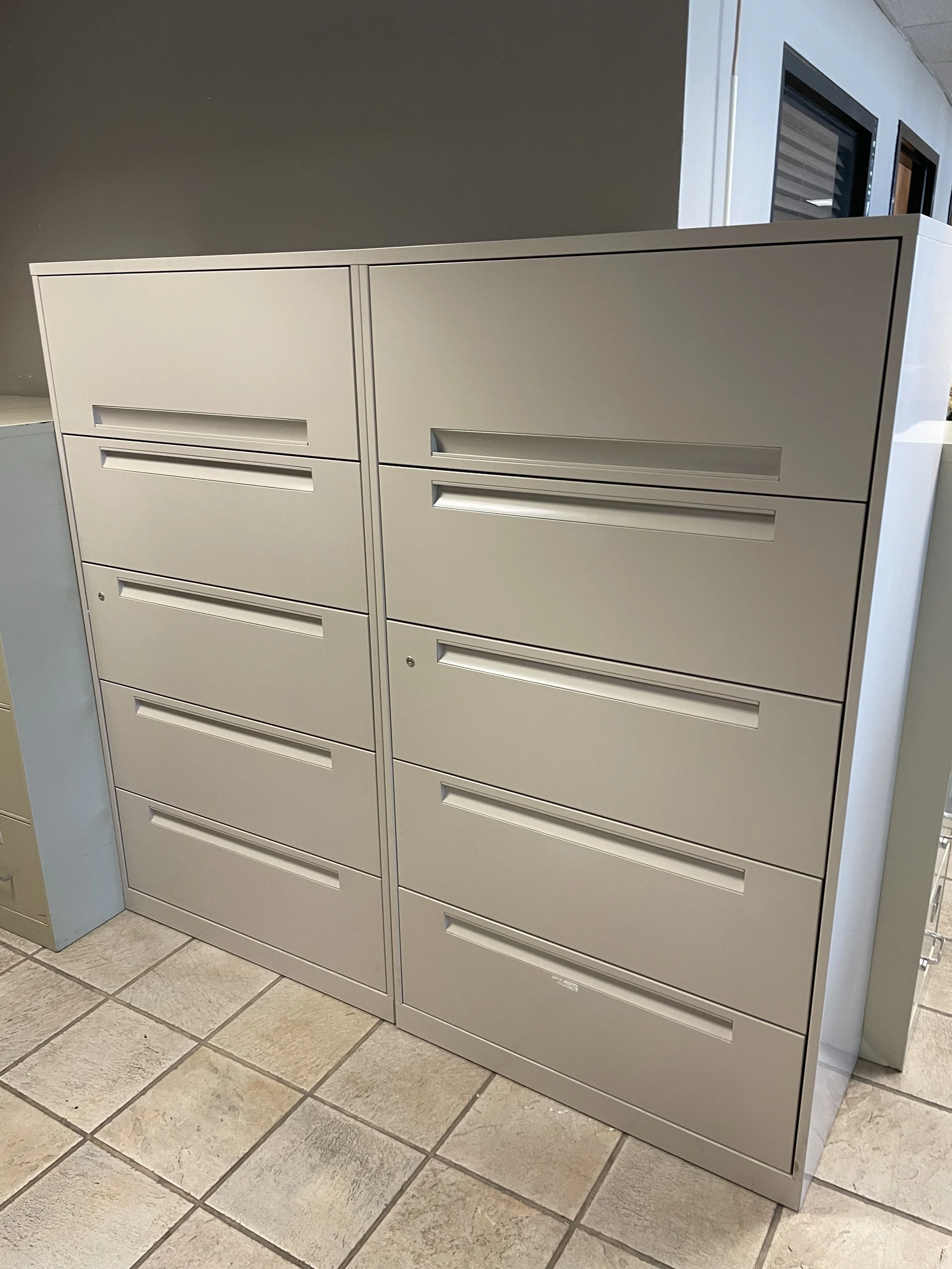 Two beige metal file cabinets with multiple drawers, situated on a tiled floor in an office setting.