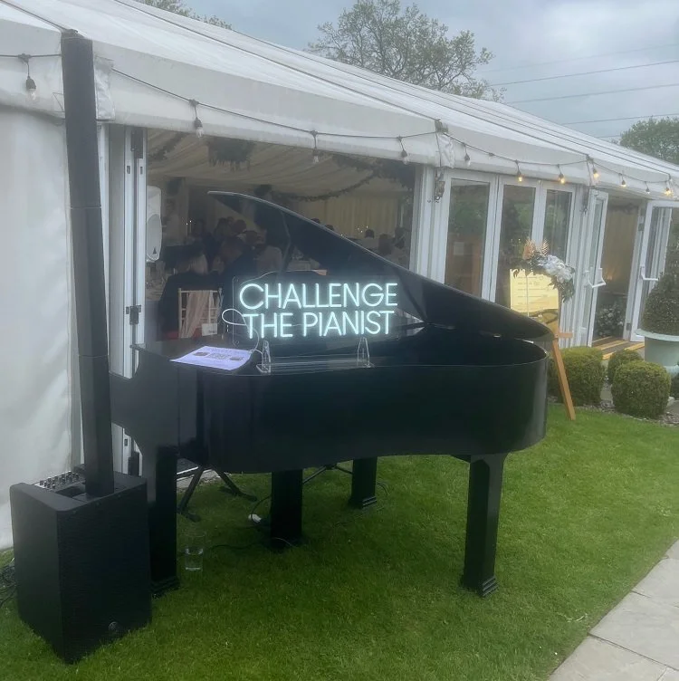Award-winning wedding pianist Chris Morris with his grand piano at Hilltop Country House. The image shows his 'challenge the pianist' neon sign on top of the piano