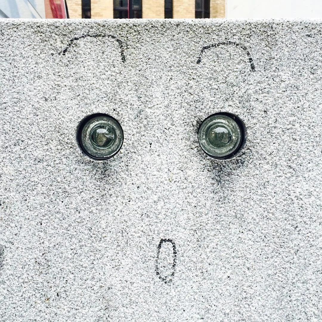 A concrete surface with two small light fixtures resembling eyes and a small vertical line beneath them resembling a surprised face.