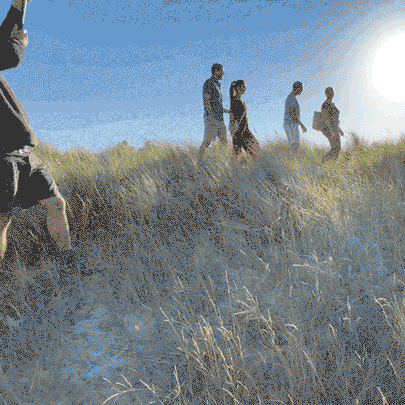 A group of friends walking along a grassy coastal dune under a bright sun.
